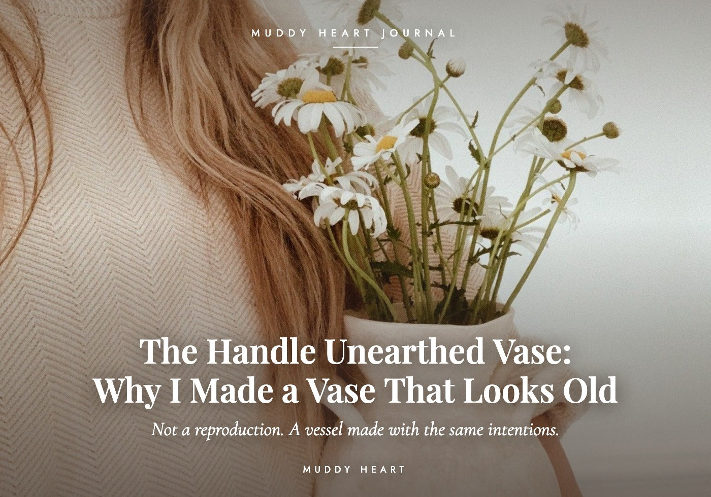 The cream Handle Unearthed ceramic vase held against a knit sweater, its two handles visible, filled with white daisies on slender green stems
