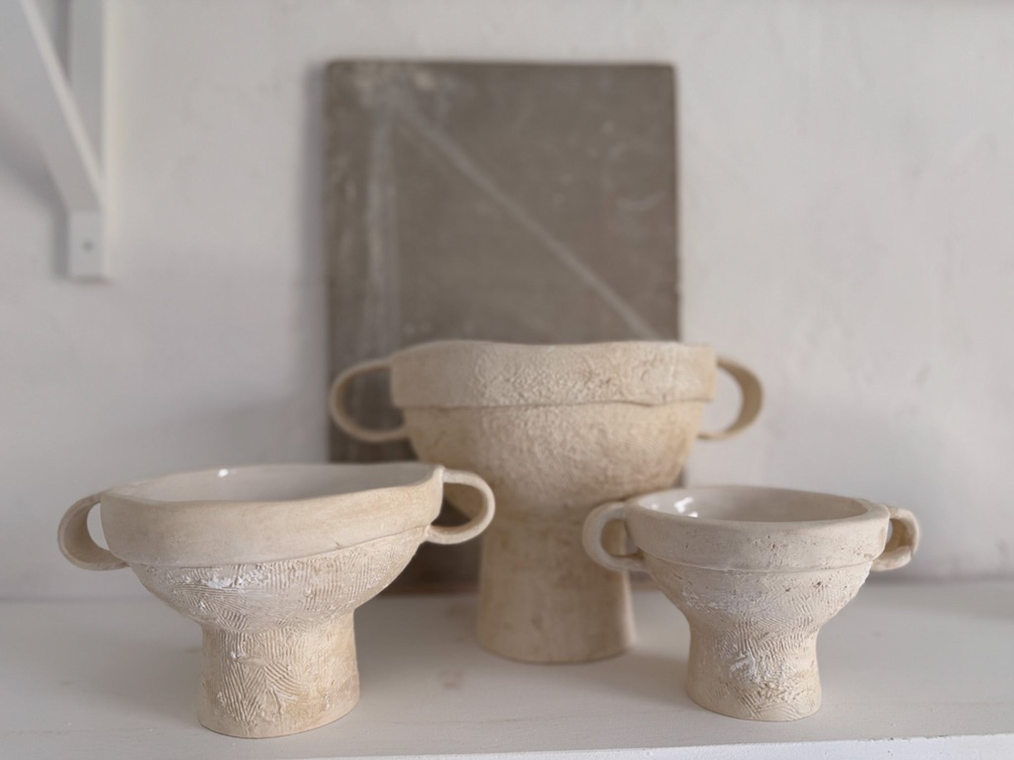 Handmade ceramic bowl with ring handles and a pedestal base in an ancient-inspired sculptural form.
