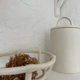 Detail of the sweeping arch handle on a handmade ceramic canister lid, shown on a white kitchen shelf.