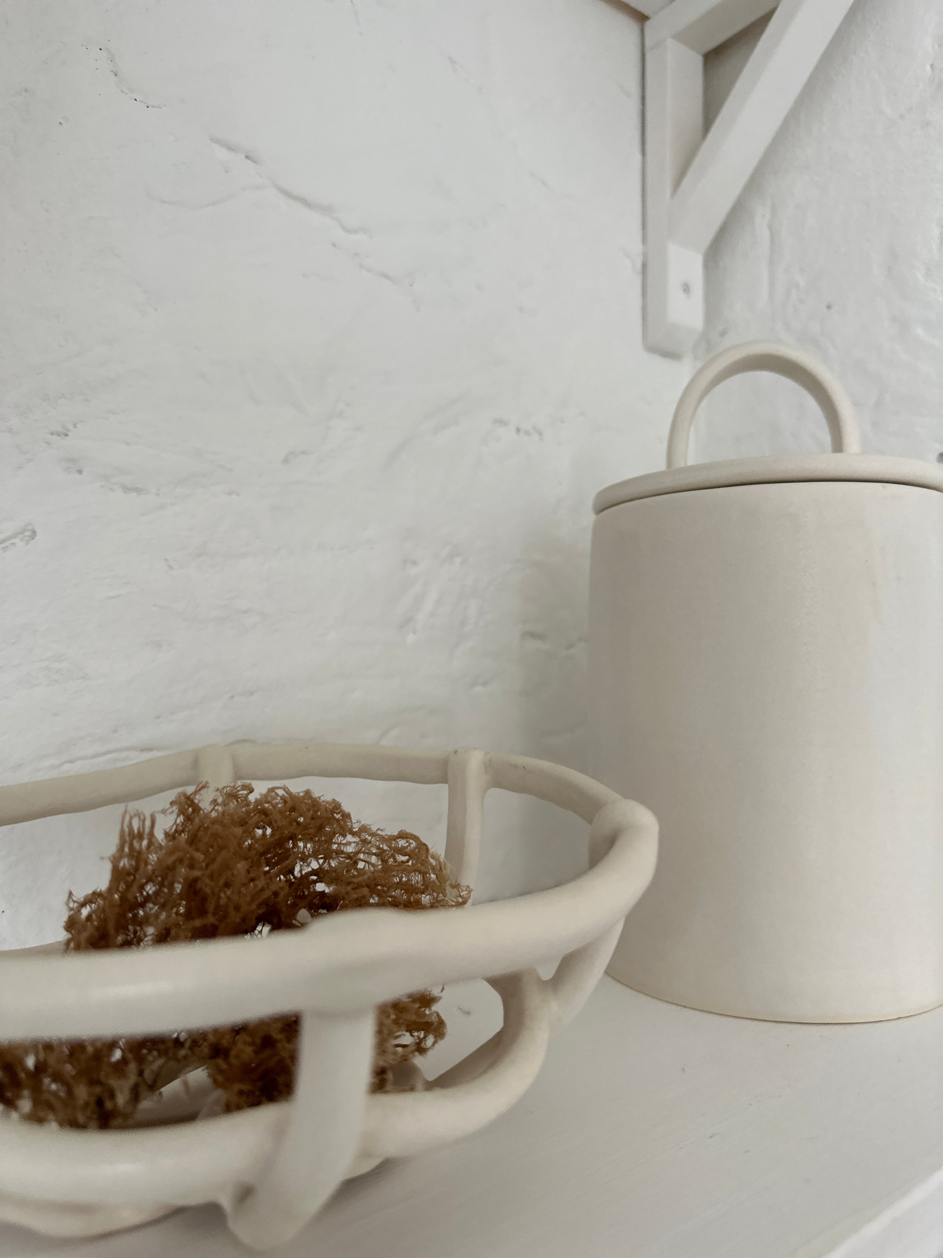 Detail of the sweeping arch handle on a handmade ceramic canister lid, shown on a white kitchen shelf.