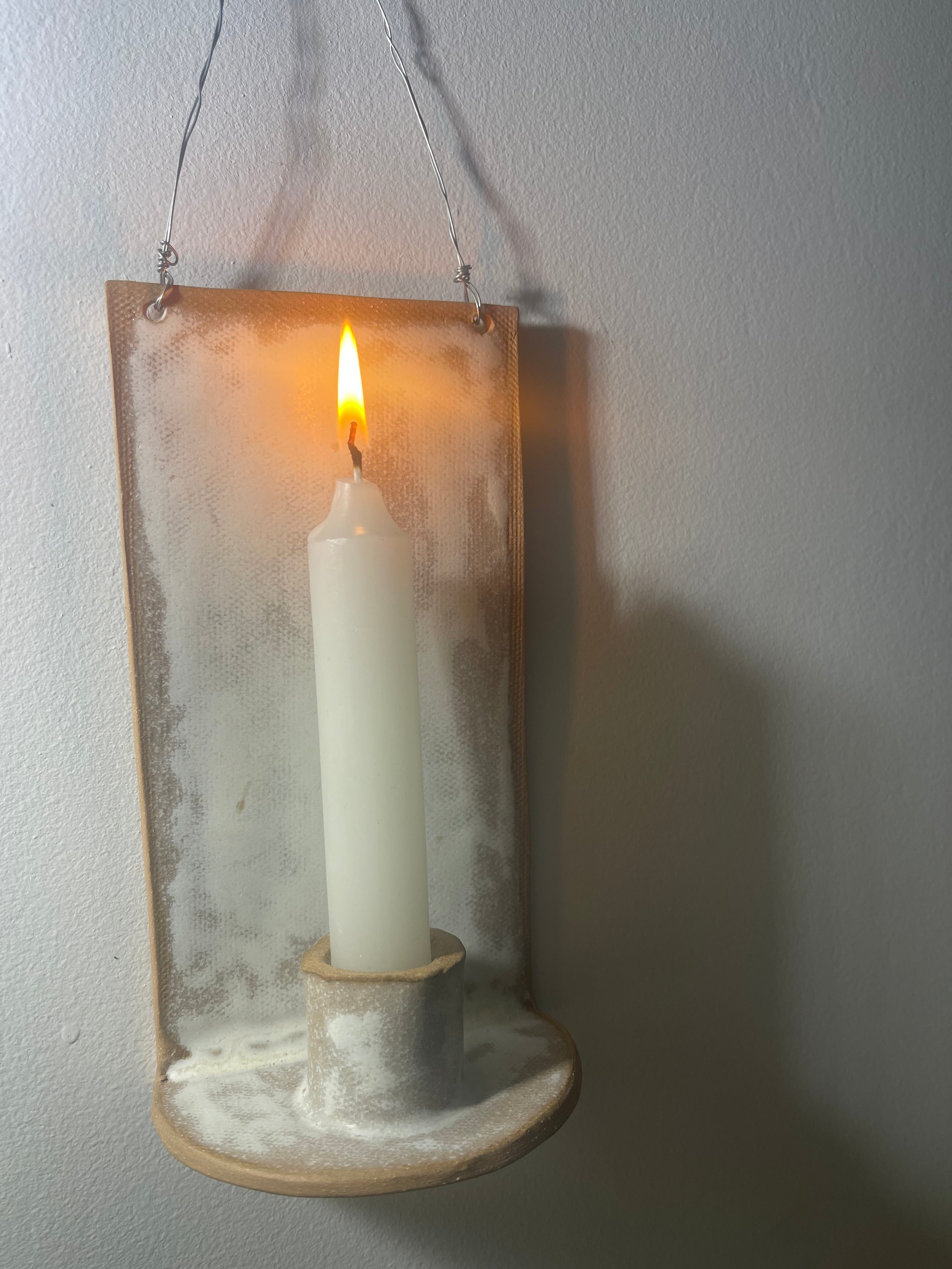 Handmade stoneware wall sconce holding a taper candle, hung from wire