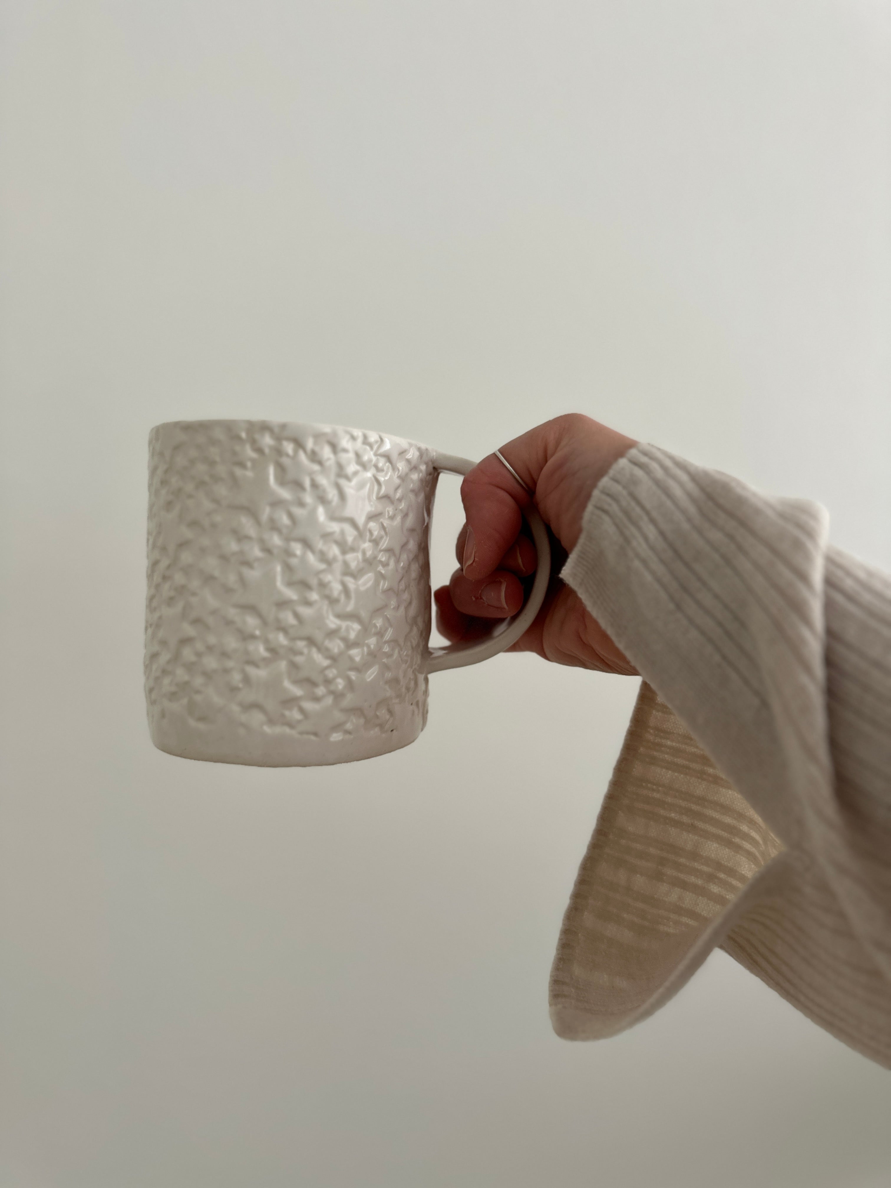 Handmade ceramic star mug held in hand, showing its wide, cozy form