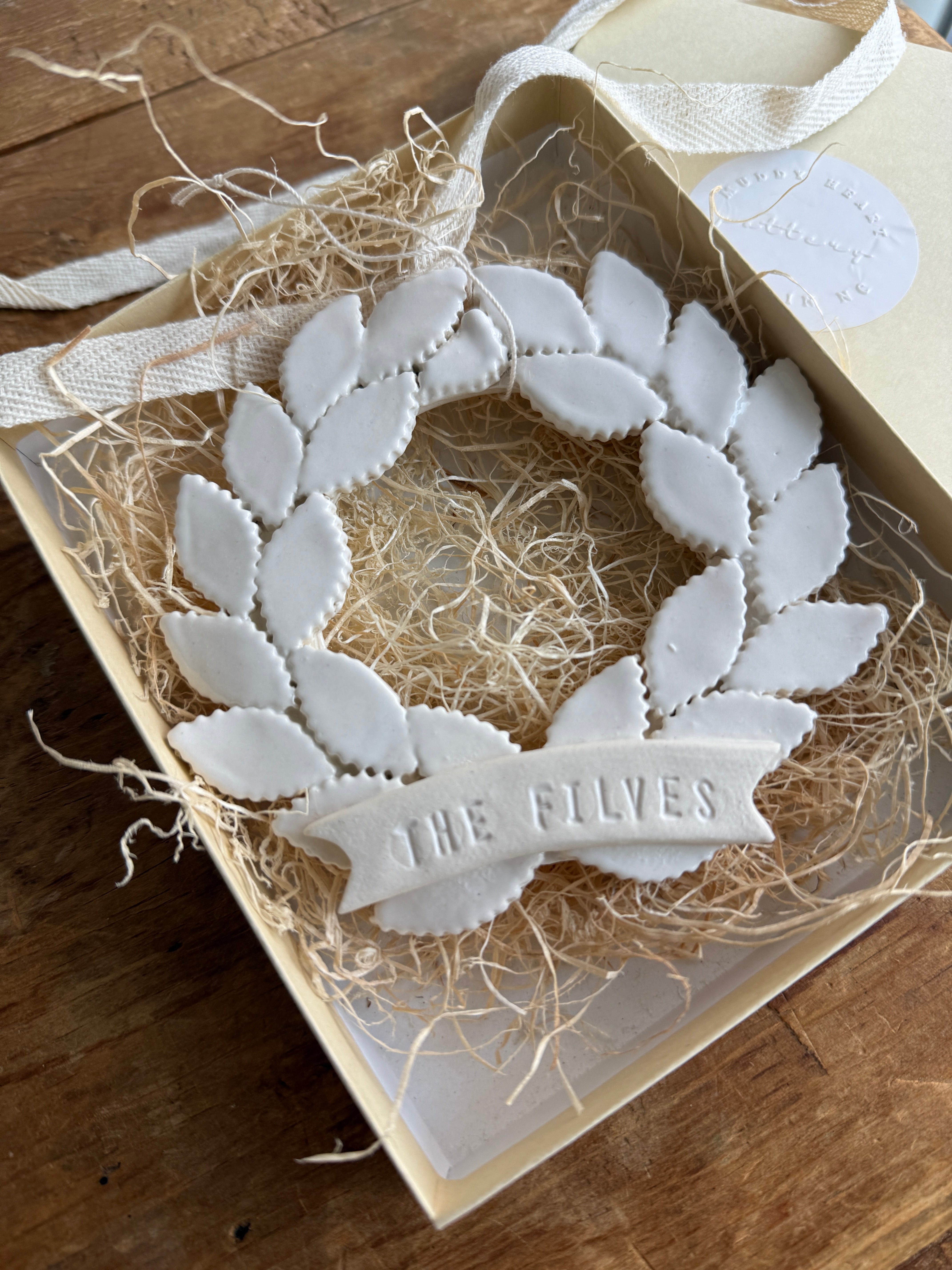 Personalized porcelain laurel wreath ornament with a gloss-white glaze and custom name on linen twine