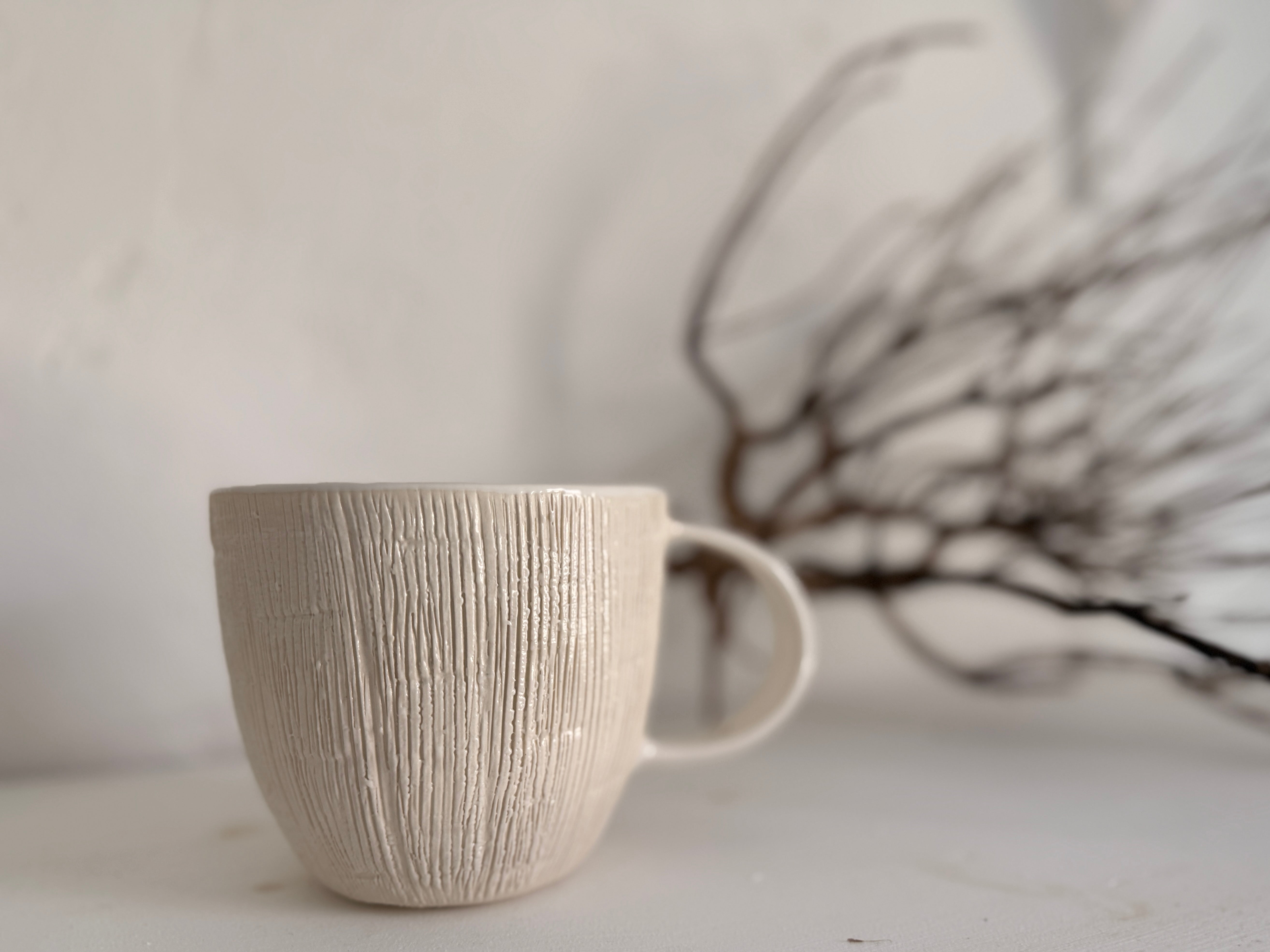 Handmade ceramic mug with deep carved vertical lines and a textured neutral glaze.