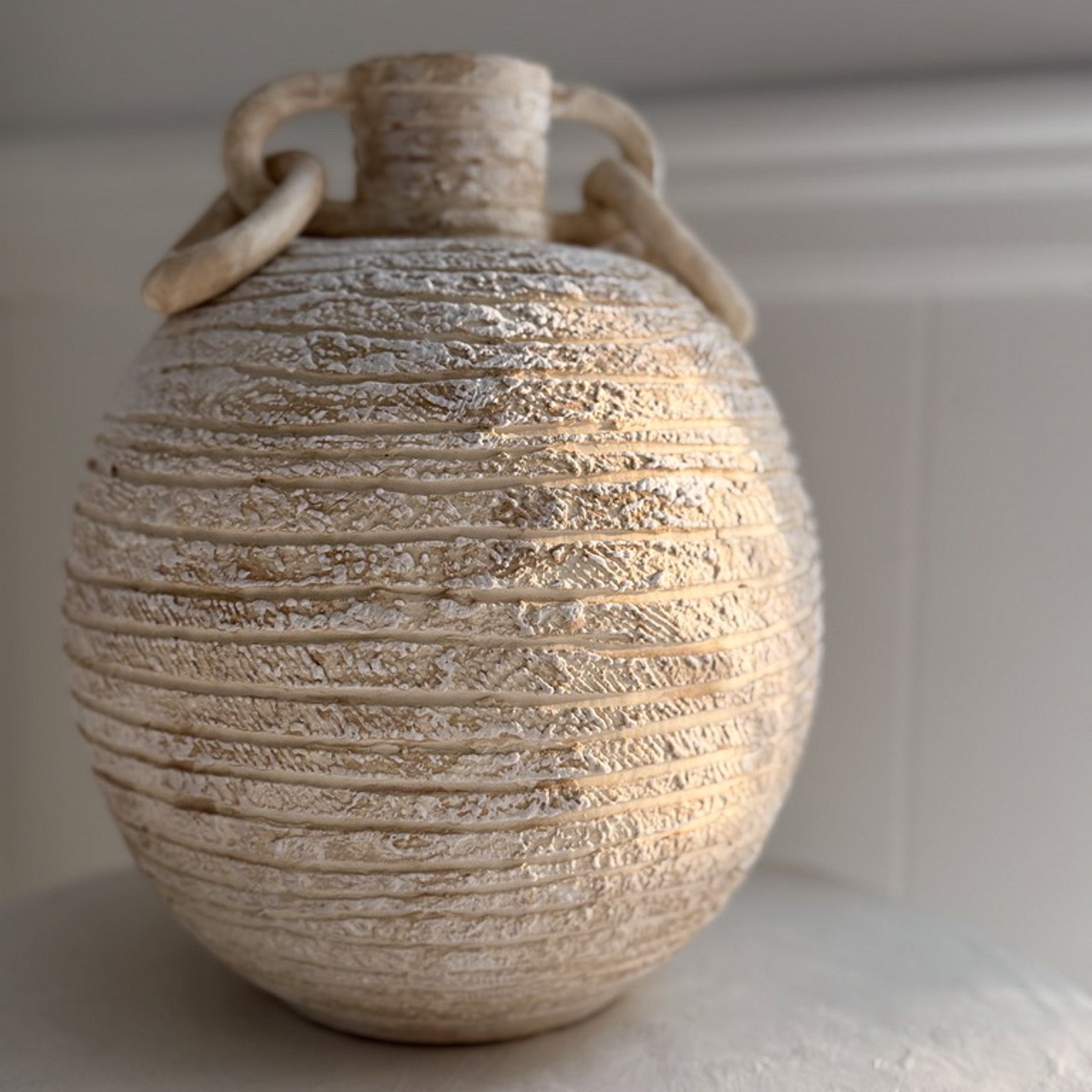Handmade globe-shaped ceramic vessel with sculptural ring handles, glazed inside and out in a neutral finish.