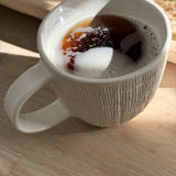 Handmade ceramic mug with deep carved vertical lines and a textured neutral glaze.