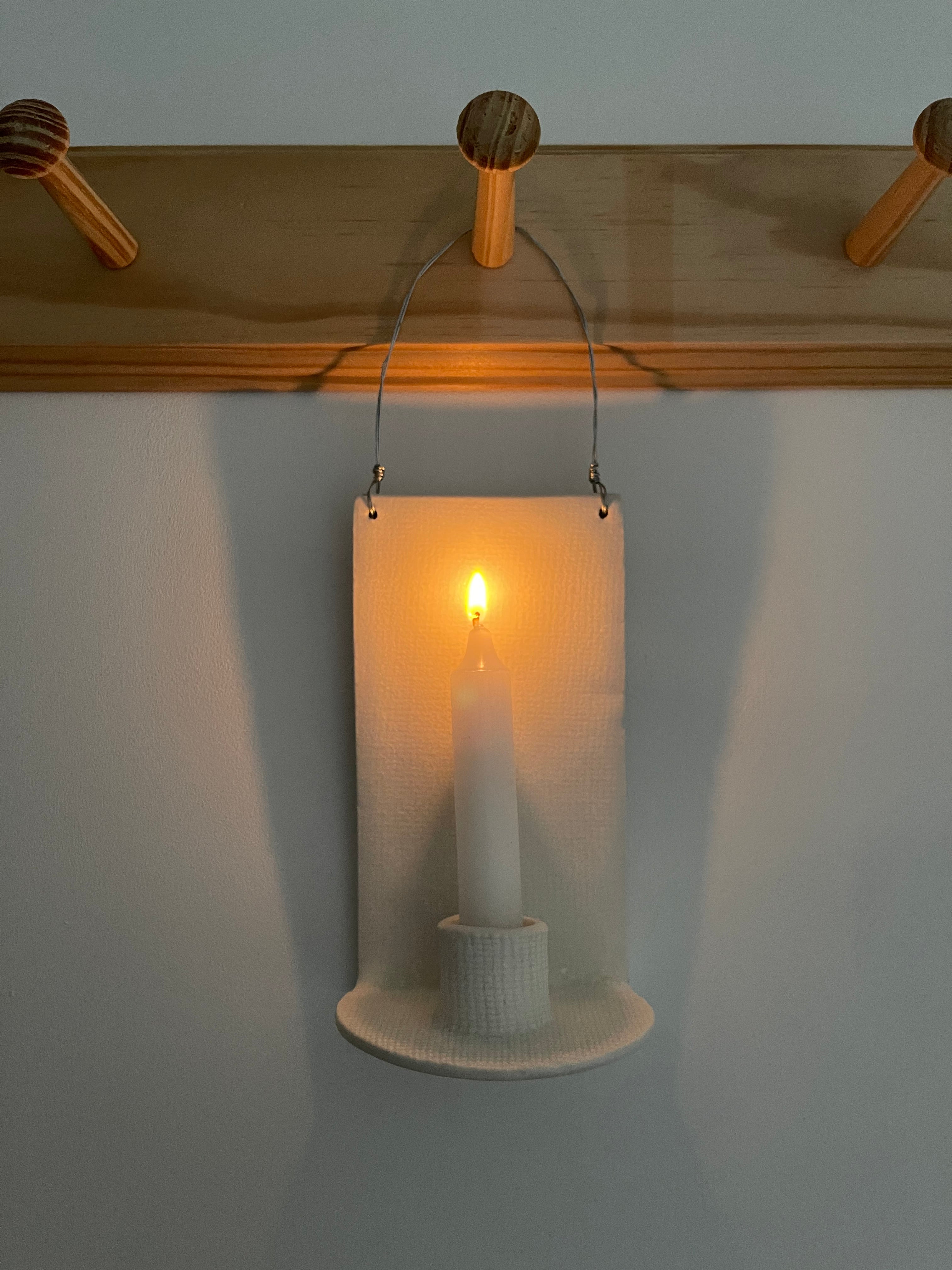 Handmade stoneware wall sconce holding a taper candle, hung from wire