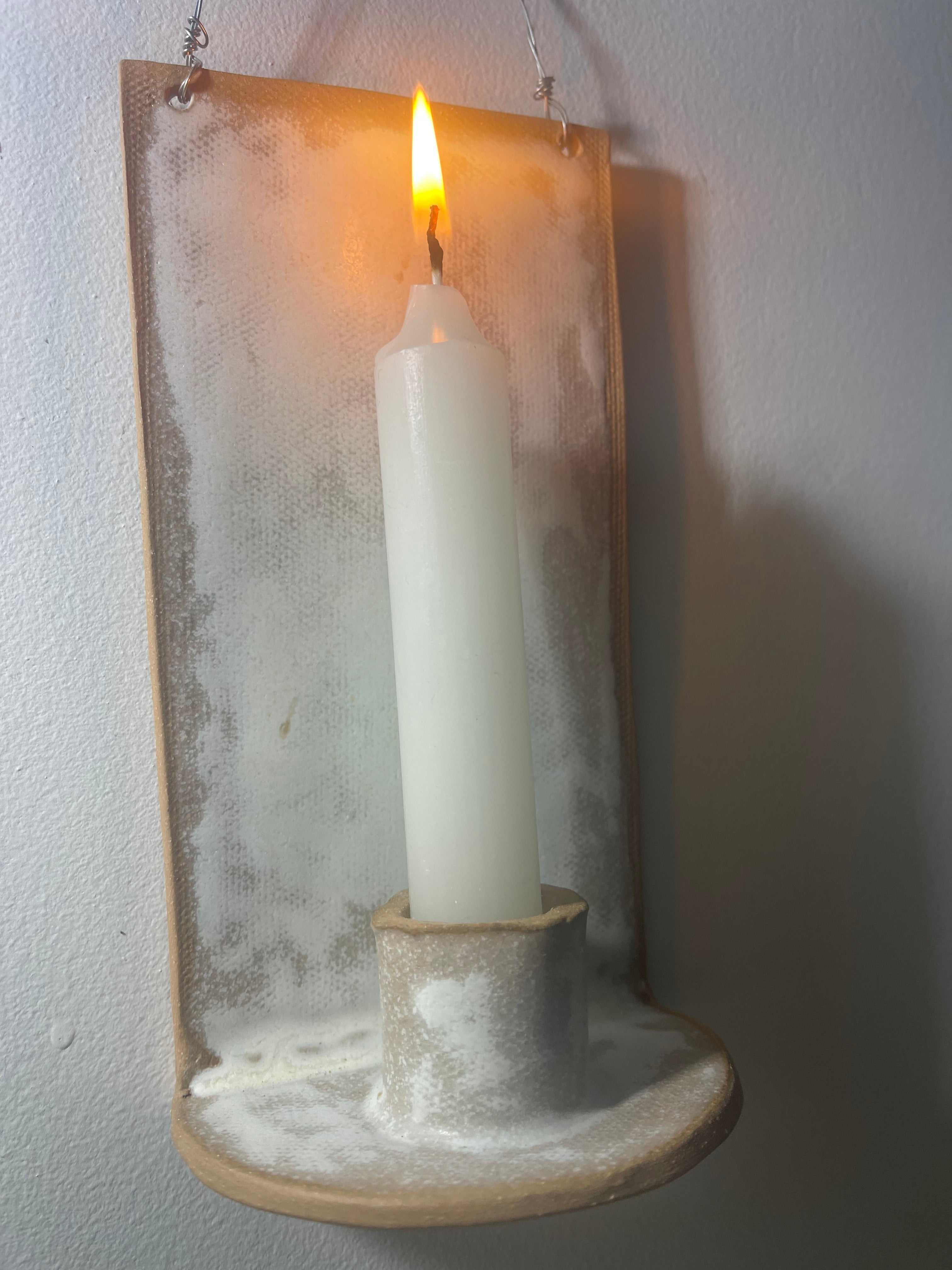 Handmade stoneware wall sconce holding a taper candle, hung from wire