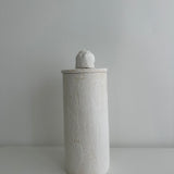 Single tall handmade ceramic canister in matte textured white with a rounded knob lid, shown against a plain pale background.
