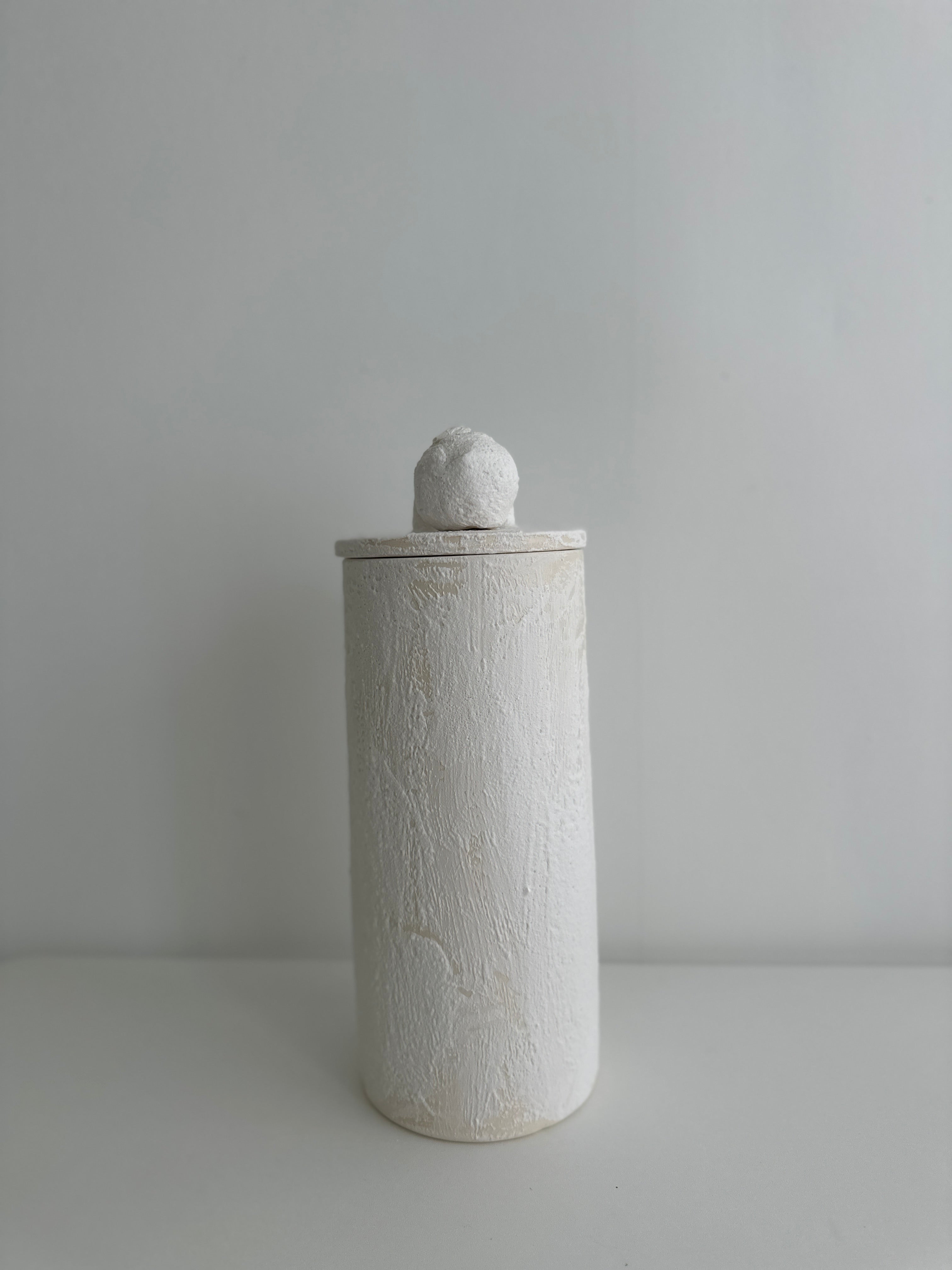 Single tall handmade ceramic canister in matte textured white with a rounded knob lid, shown against a plain pale background.