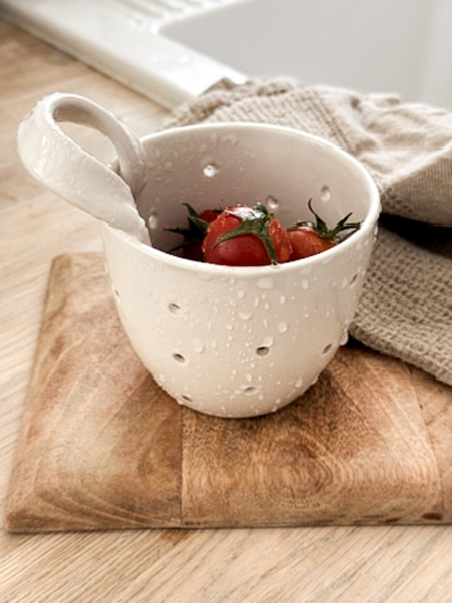 Handmade elongated ceramic berry bowl colander with drainage holes and a handle, in a neutral finish.