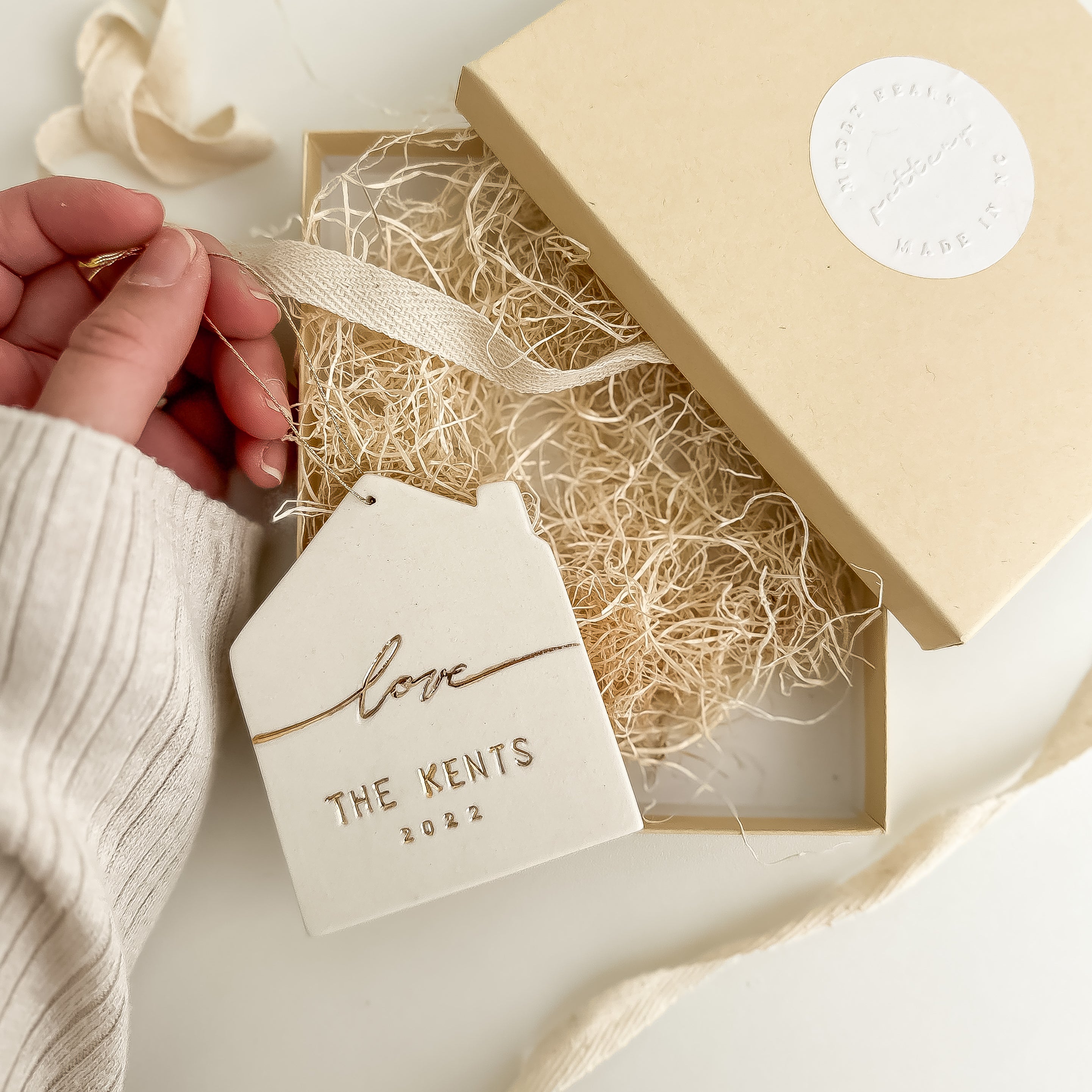 Personalized white porcelain house ornament hand-lettered with a name, hung on twine