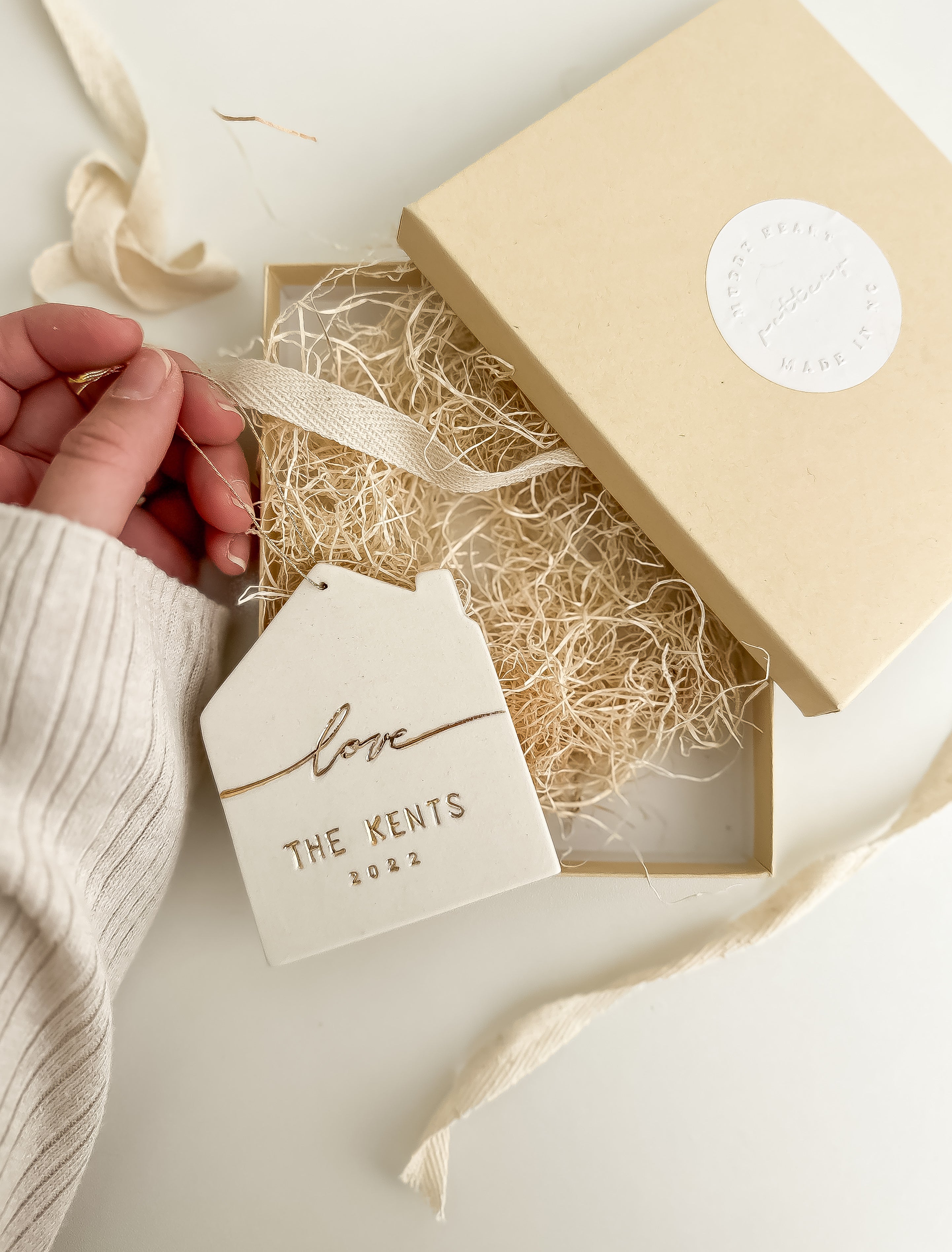 Personalized white porcelain house ornament hand-lettered with a name, hung on twine