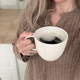 Handmade ceramic mug with deep carved vertical lines and a textured neutral glaze.