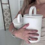 Maker holding two handmade ceramic canisters with long-arch lid handles in frost white, showing their scale in her arms.