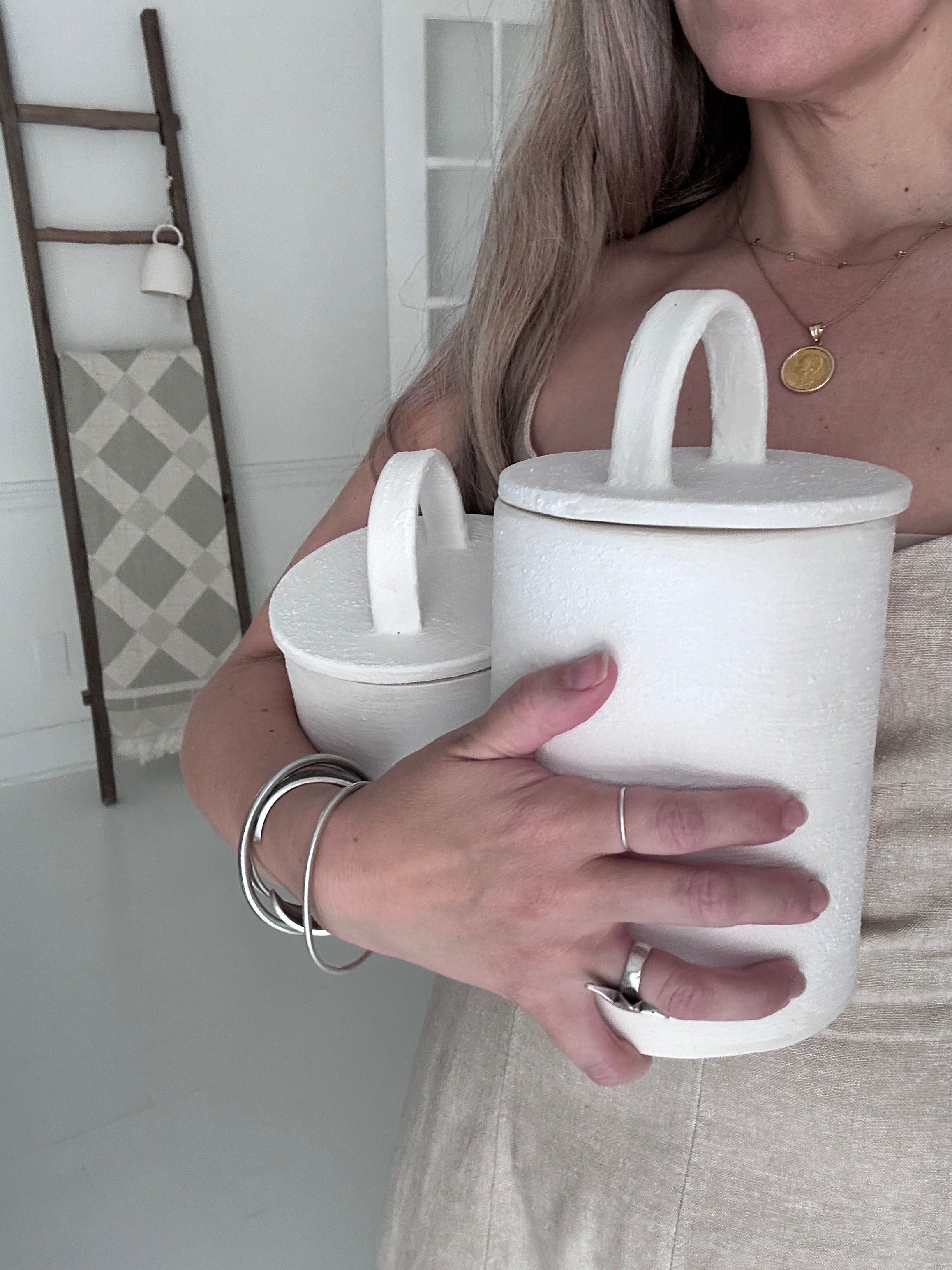 Maker holding two handmade ceramic canisters with long-arch lid handles in frost white, showing their scale in her arms.