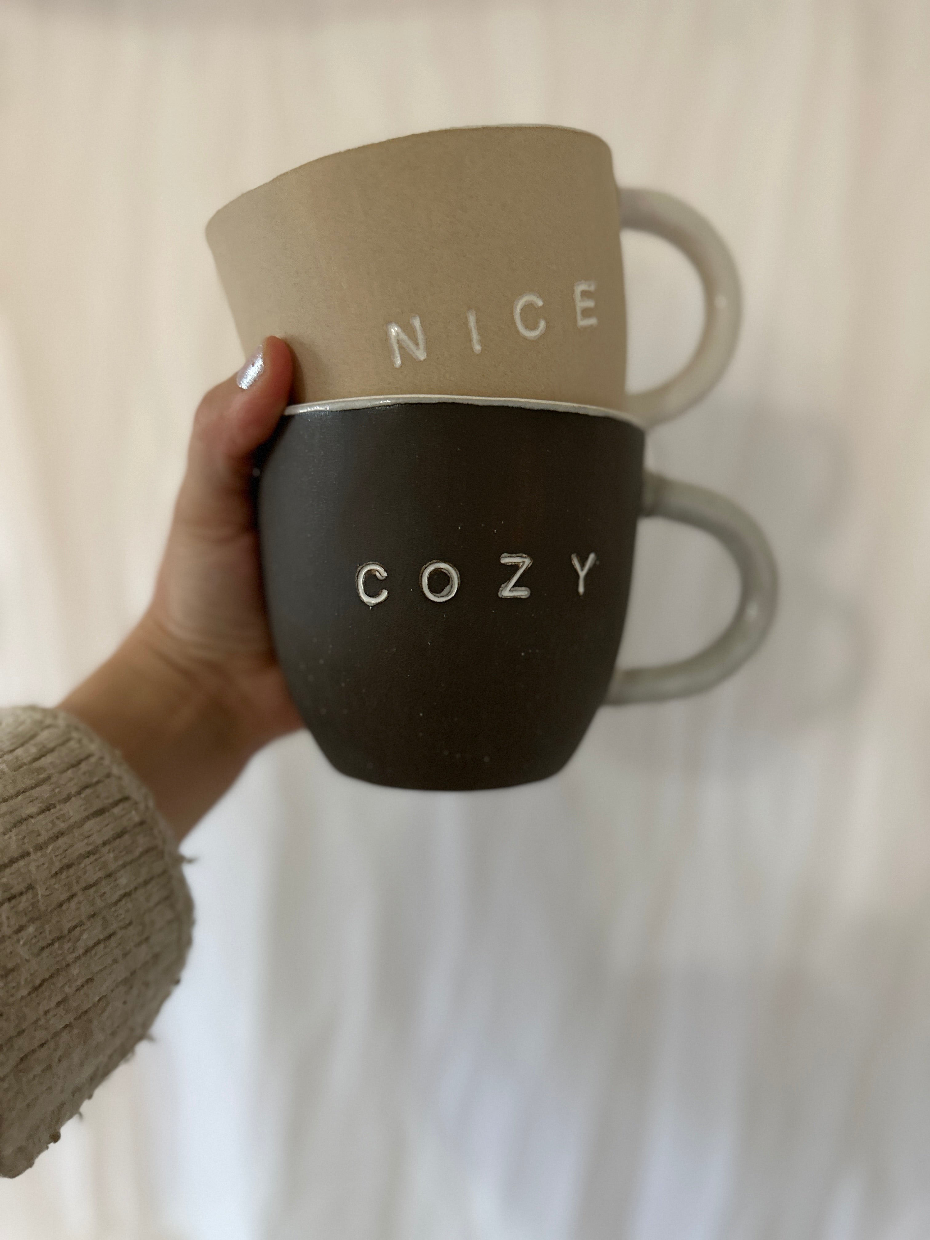 Handmade ceramic 'Nice' and 'Cozy' mug set with a clay exterior and glossy white interior.