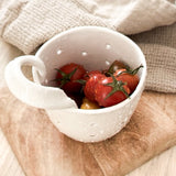 Handmade elongated ceramic berry bowl colander with drainage holes and a handle, in a neutral finish.