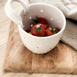 Handmade elongated ceramic berry bowl colander with drainage holes and a handle, in a neutral finish.