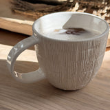 Handmade ceramic mug with deep carved vertical lines and a textured neutral glaze.