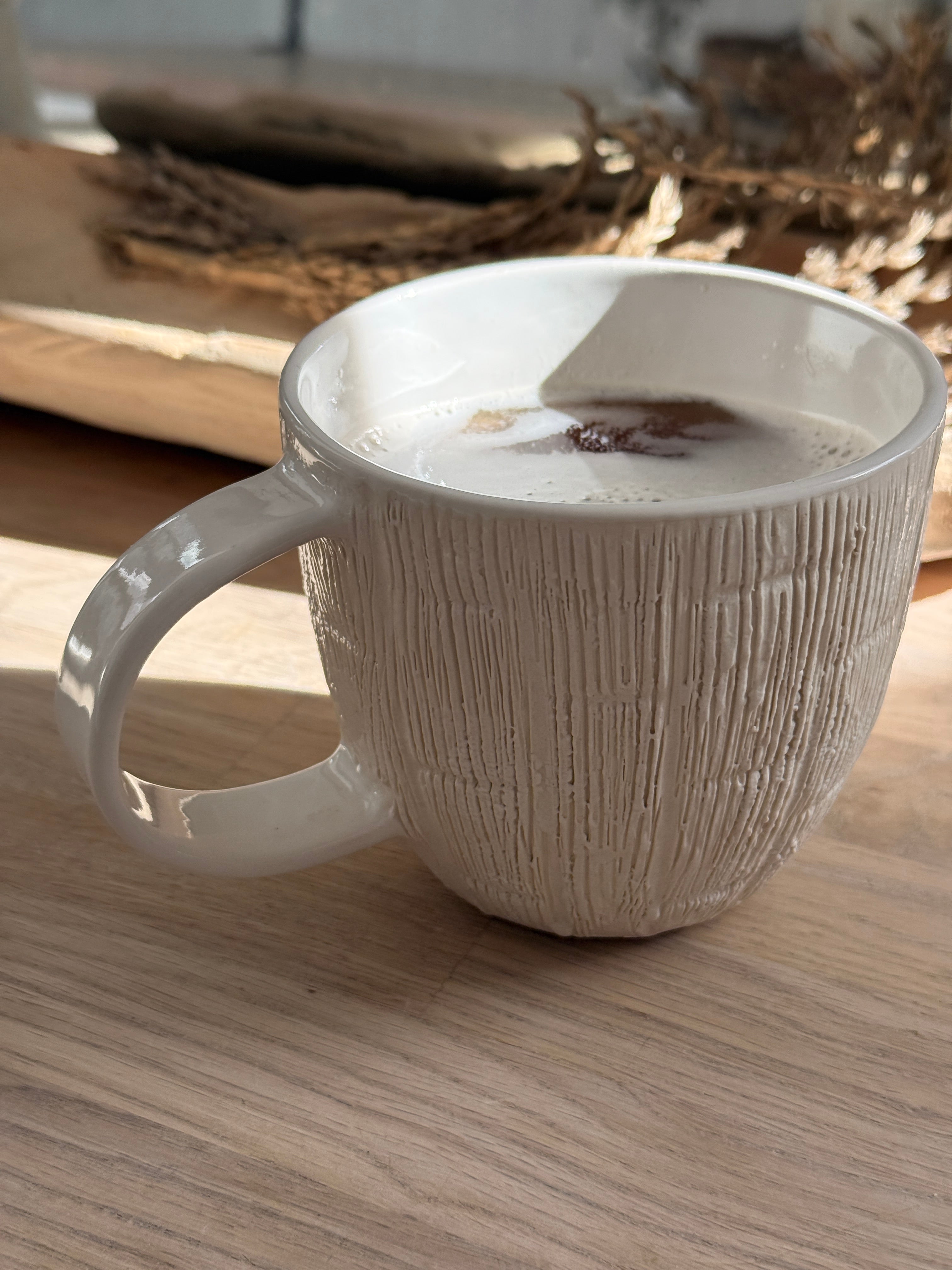 Handmade ceramic mug with deep carved vertical lines and a textured neutral glaze.