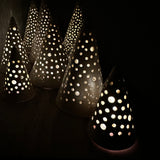 Handmade white stoneware tree luminaries with star cutouts glowing with LED tealight candles