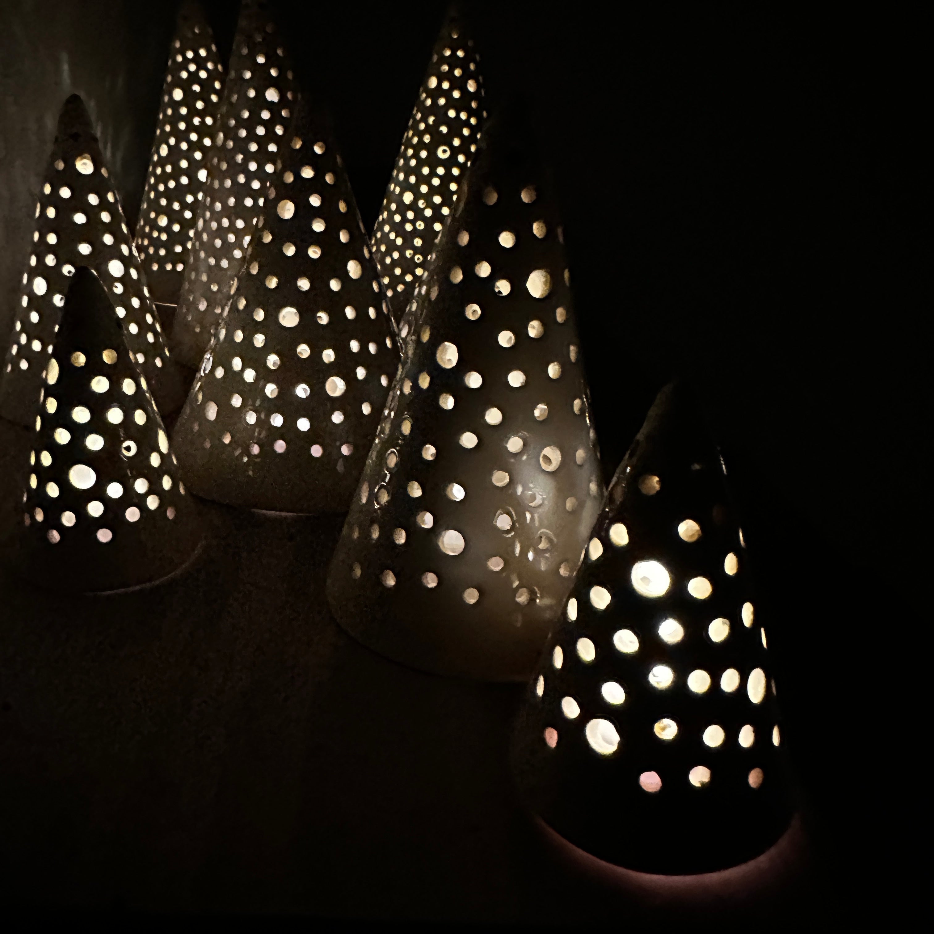 Handmade white stoneware tree luminaries with star cutouts glowing with LED tealight candles