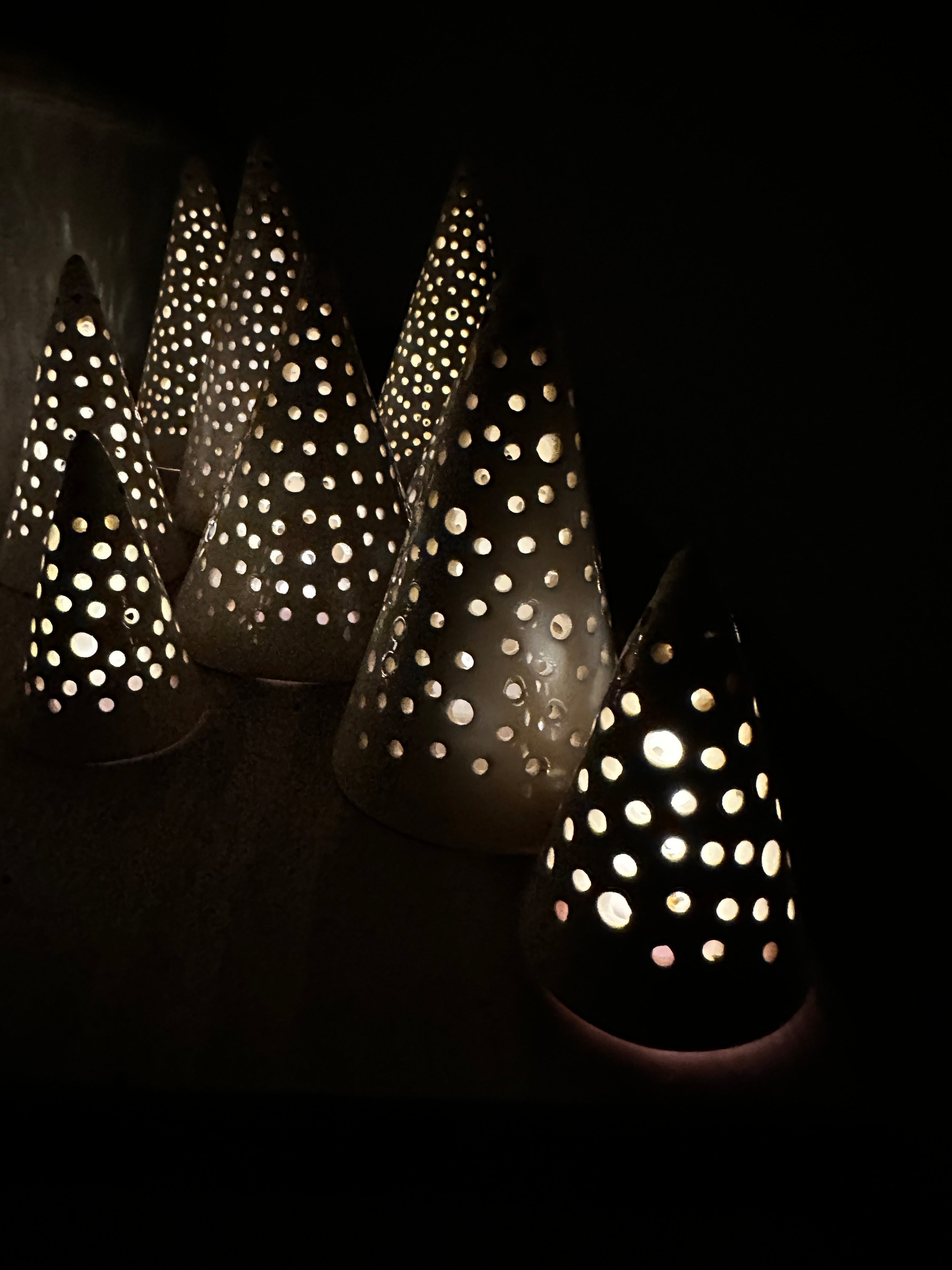Handmade white stoneware tree luminaries with star cutouts glowing with LED tealight candles