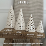 Handmade white stoneware tree luminaries with star cutouts glowing with LED tealight candles