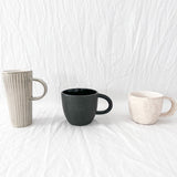 Assorted handmade ceramic mugs with textured glazes, dishwasher-safe seconds-sale pieces from Muddy Heart