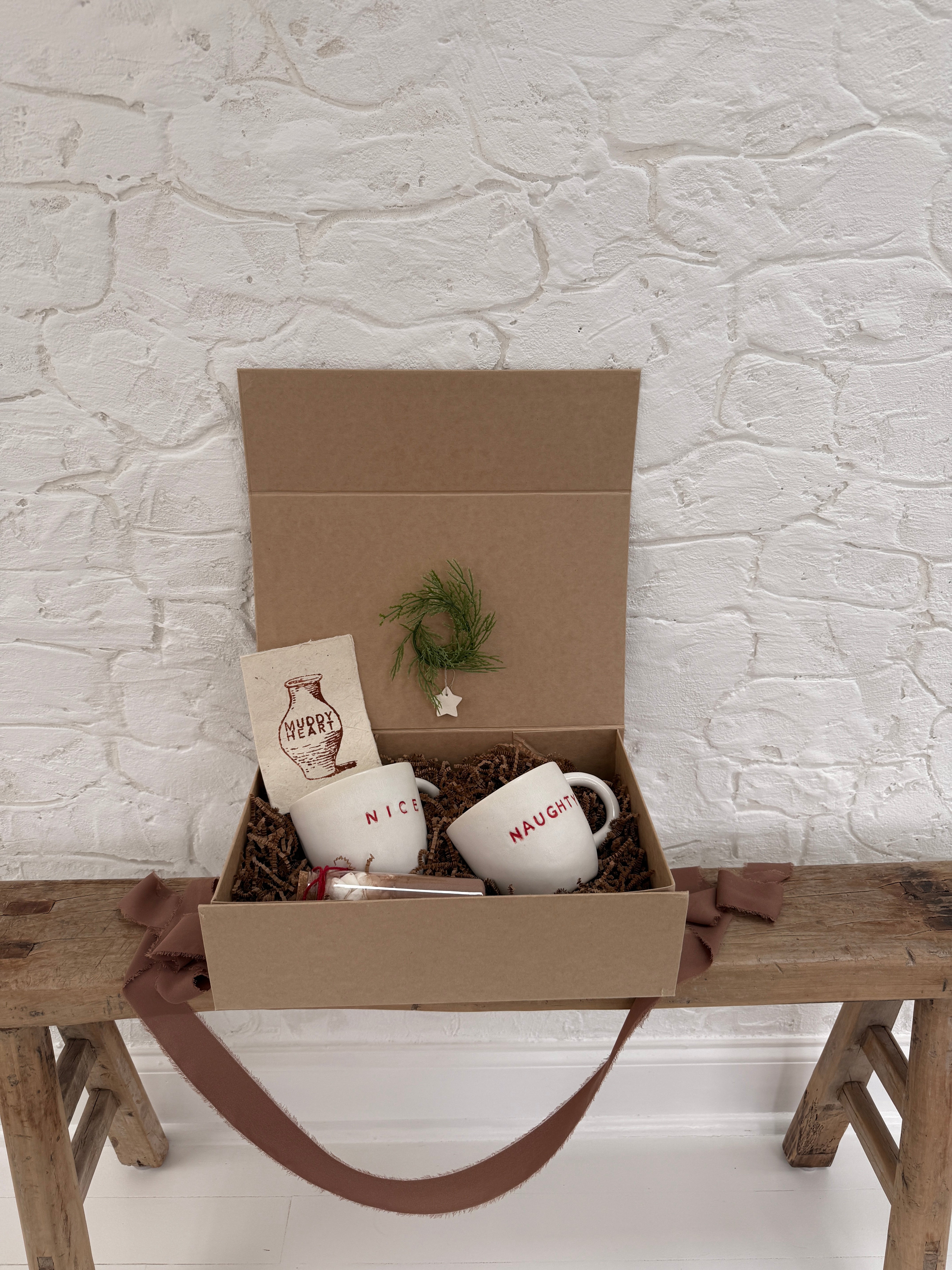 Pair of handmade ceramic mugs reading Naughty and Nice, paired with a hot cocoa and marshmallow mix.