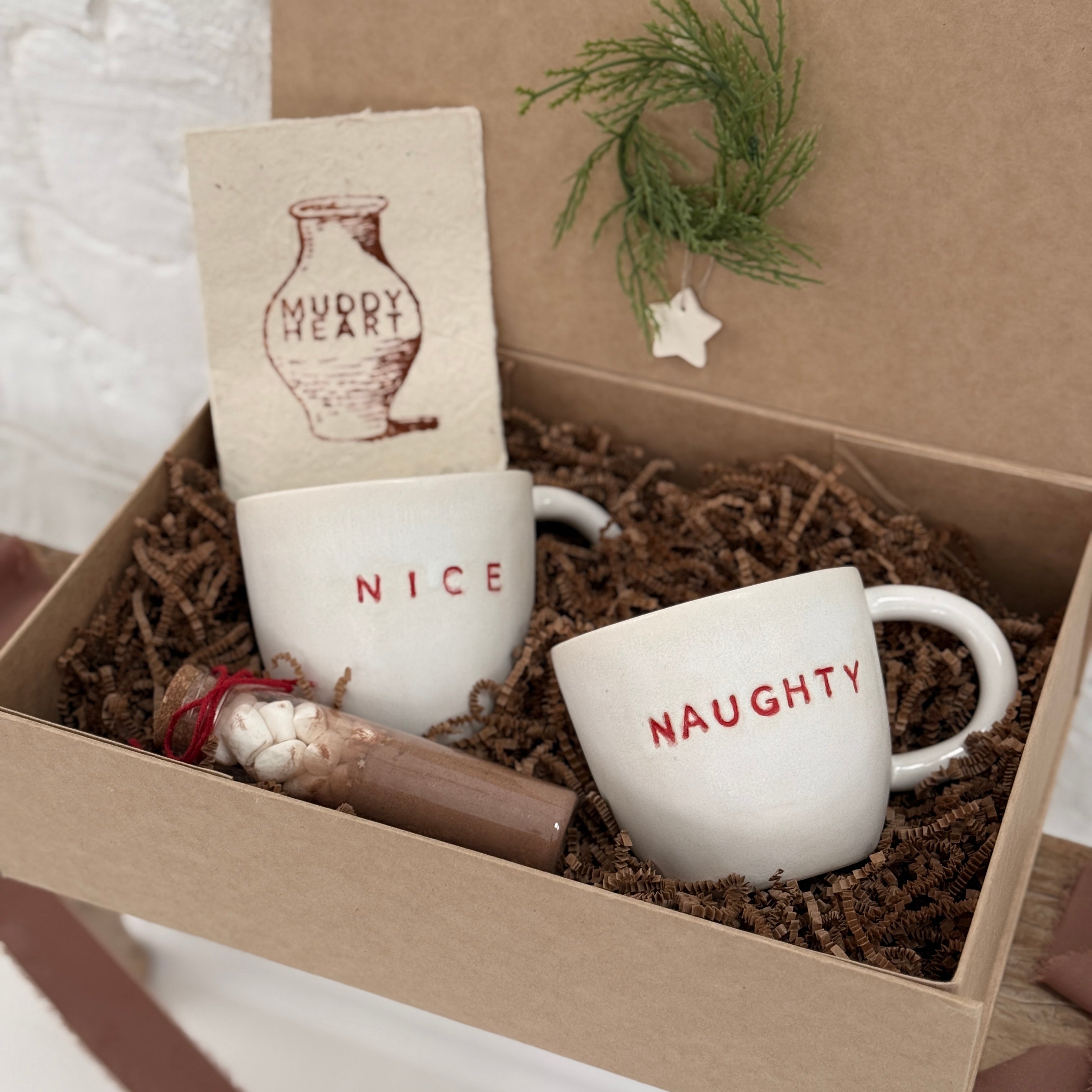 Pair of handmade ceramic mugs reading Naughty and Nice, paired with a hot cocoa and marshmallow mix.