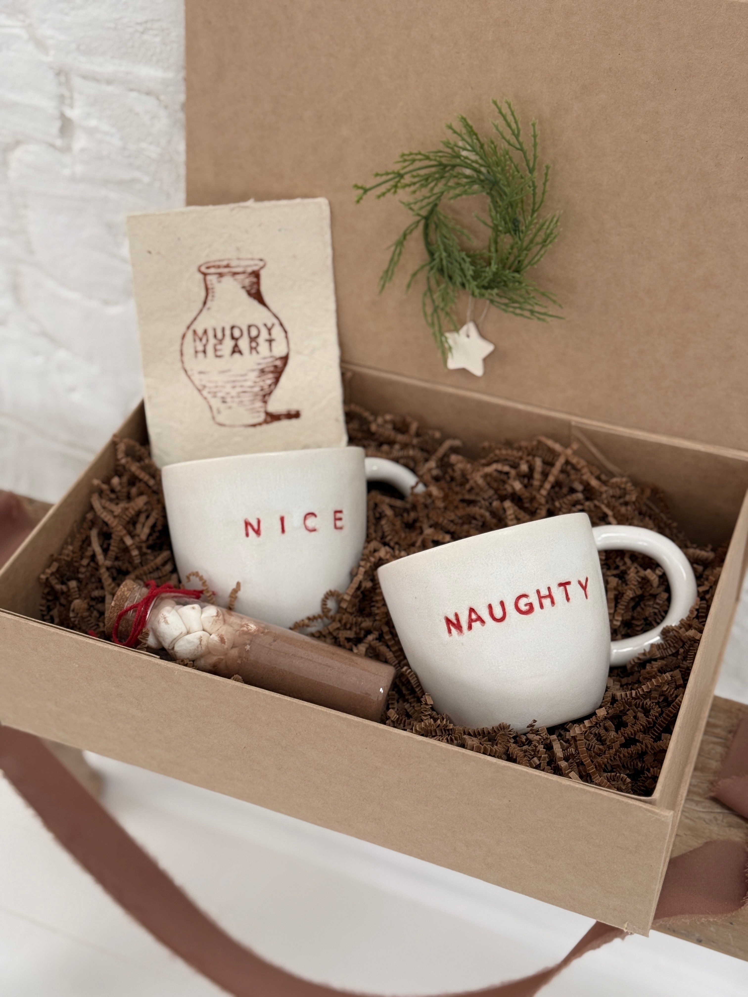 Pair of handmade ceramic mugs reading Naughty and Nice, paired with a hot cocoa and marshmallow mix.