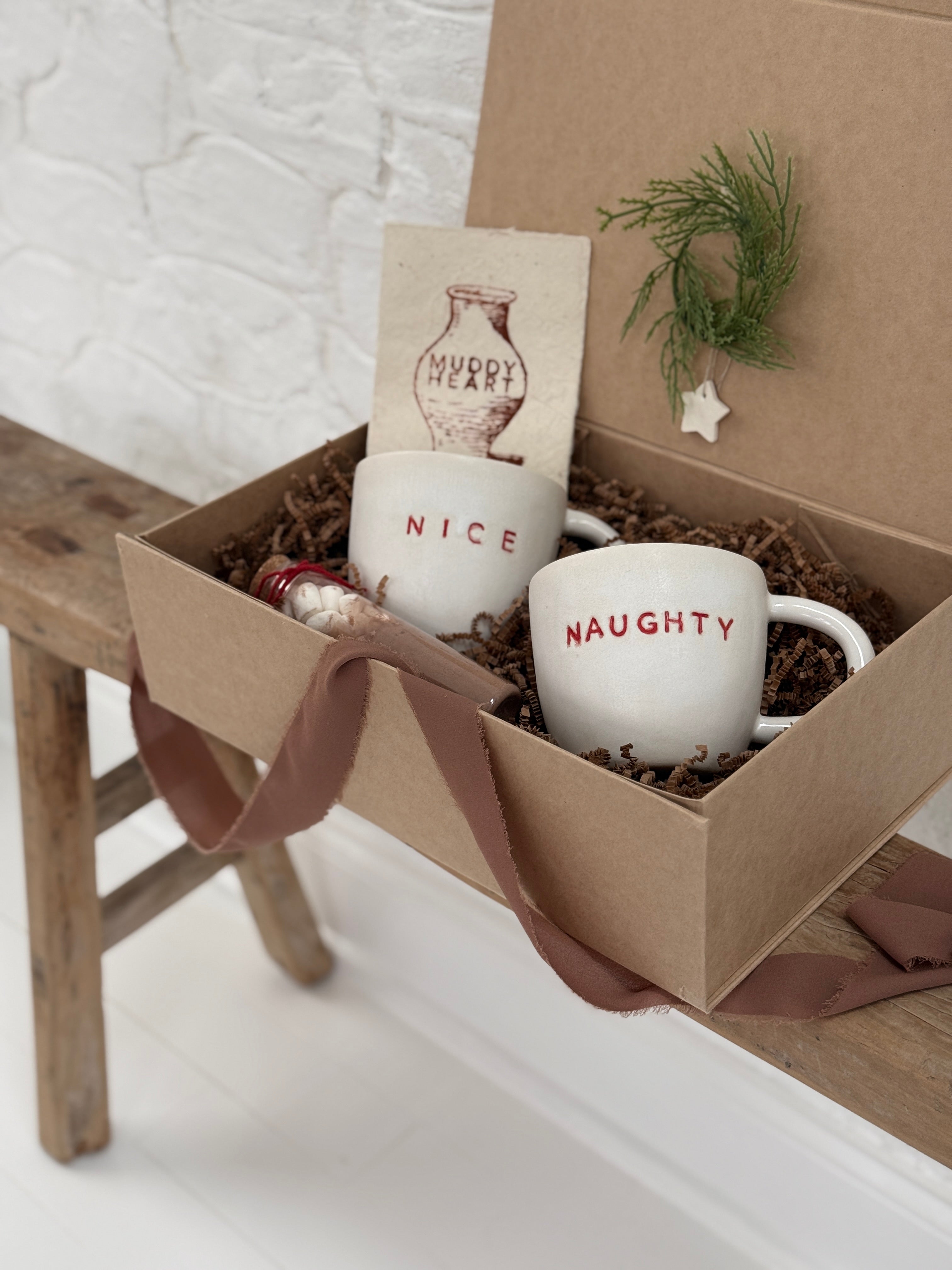 Pair of handmade ceramic mugs reading Naughty and Nice, paired with a hot cocoa and marshmallow mix.