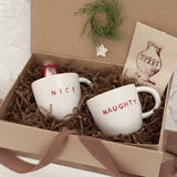 Pair of handmade ceramic mugs reading Naughty and Nice, paired with a hot cocoa and marshmallow mix.