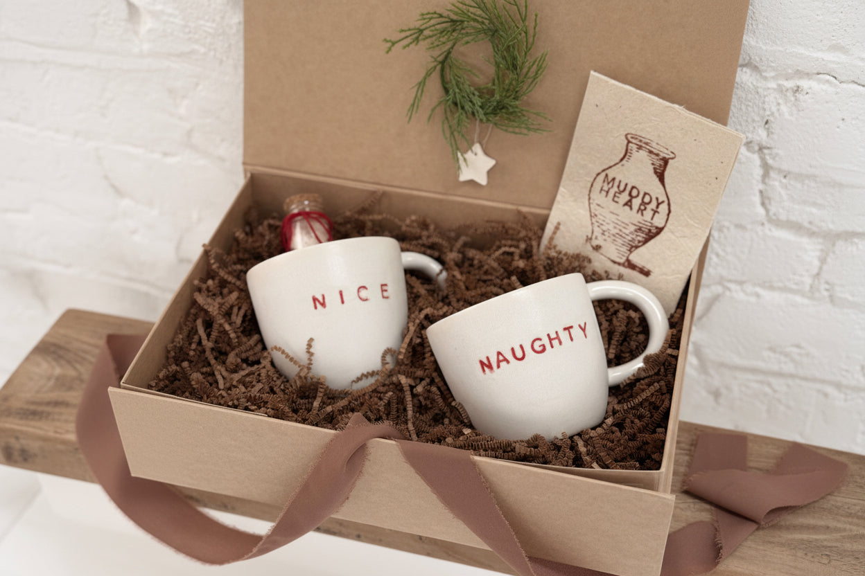 Pair of handmade ceramic mugs reading Naughty and Nice, paired with a hot cocoa and marshmallow mix.