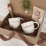 Pair of handmade ceramic mugs reading Naughty and Nice, paired with a hot cocoa and marshmallow mix.