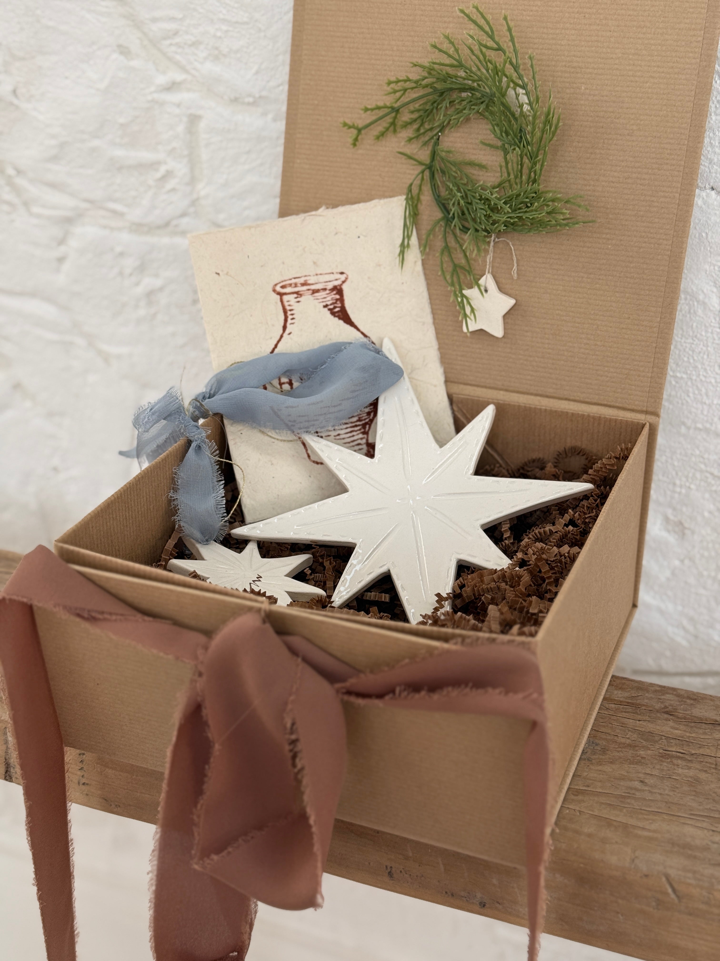 Pair of handmade glossy white ceramic North Star ornaments, one large and one small, tied with ribbon for hanging.