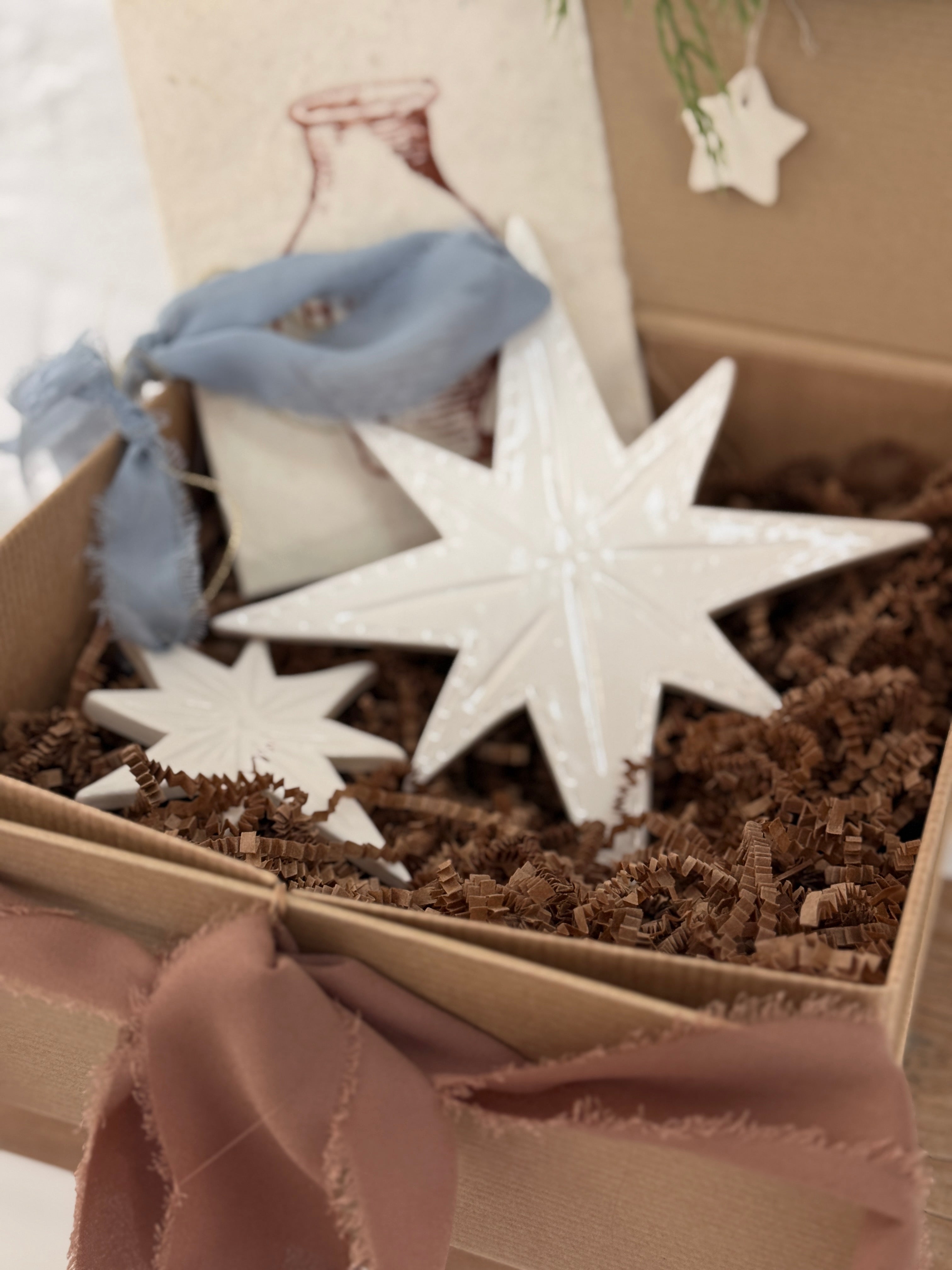 Pair of handmade glossy white ceramic North Star ornaments, one large and one small, tied with ribbon for hanging.