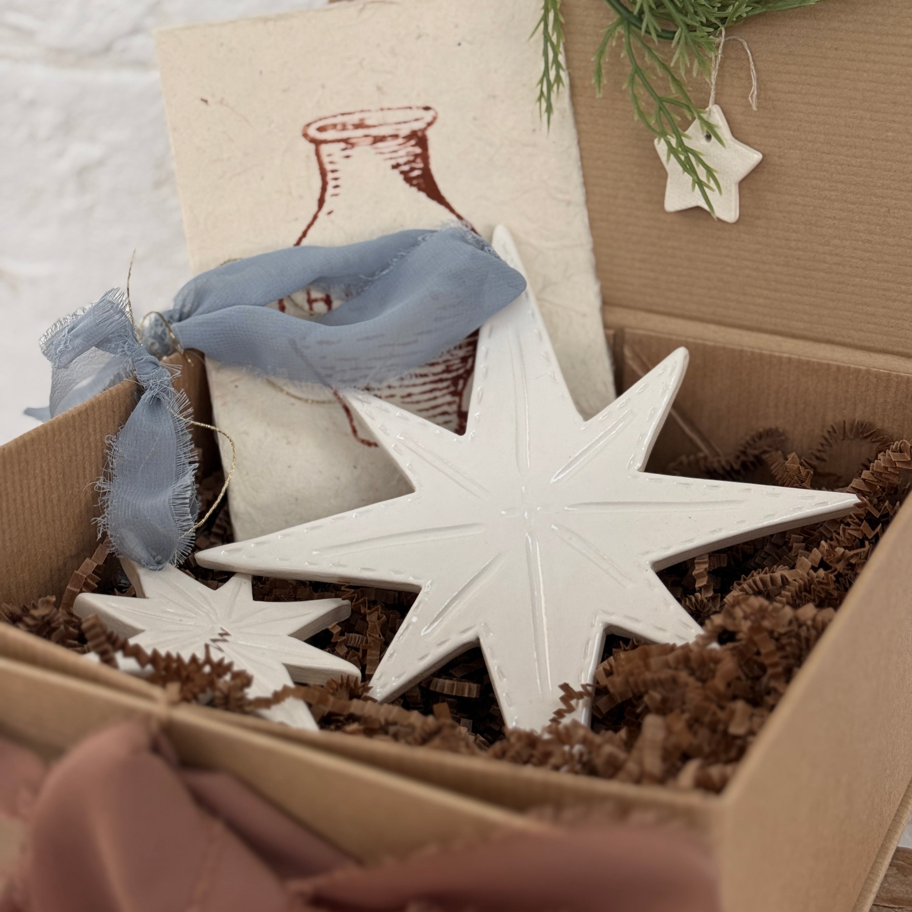 Pair of handmade glossy white ceramic North Star ornaments, one large and one small, tied with ribbon for hanging.