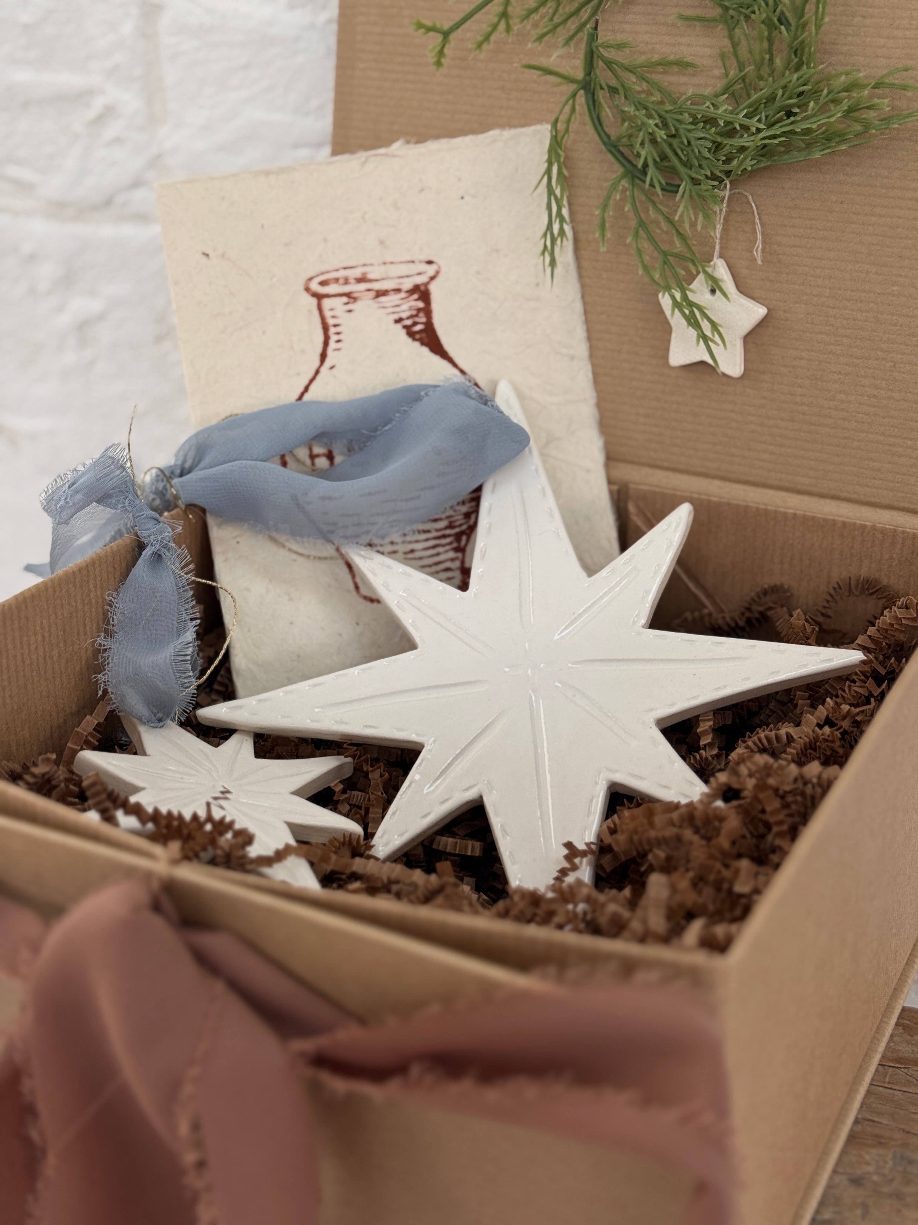 Pair of handmade glossy white ceramic North Star ornaments, one large and one small, tied with ribbon for hanging.