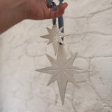 Pair of handmade glossy white ceramic North Star ornaments, one large and one small, tied with ribbon for hanging.