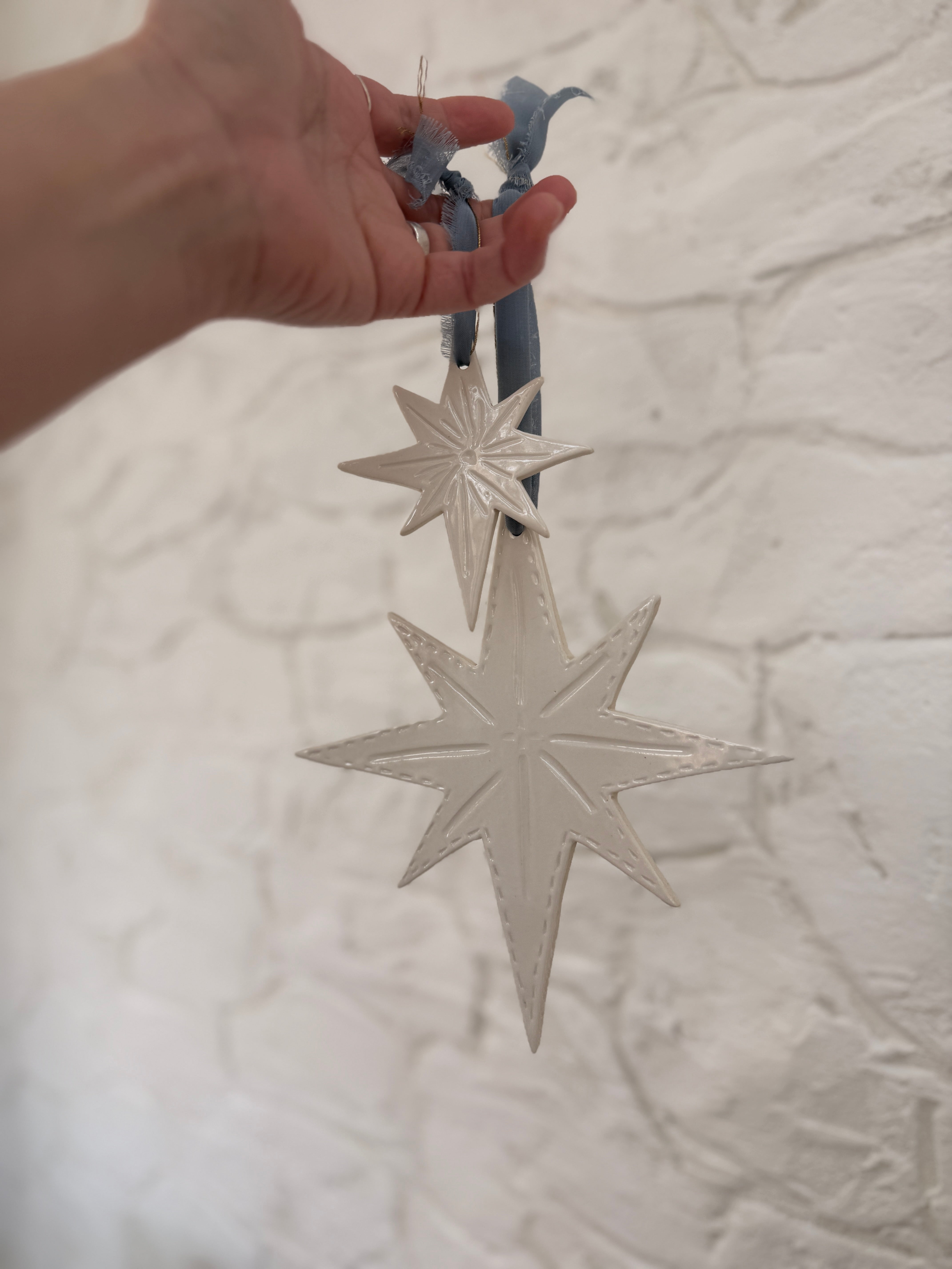 Pair of handmade glossy white ceramic North Star ornaments, one large and one small, tied with ribbon for hanging.