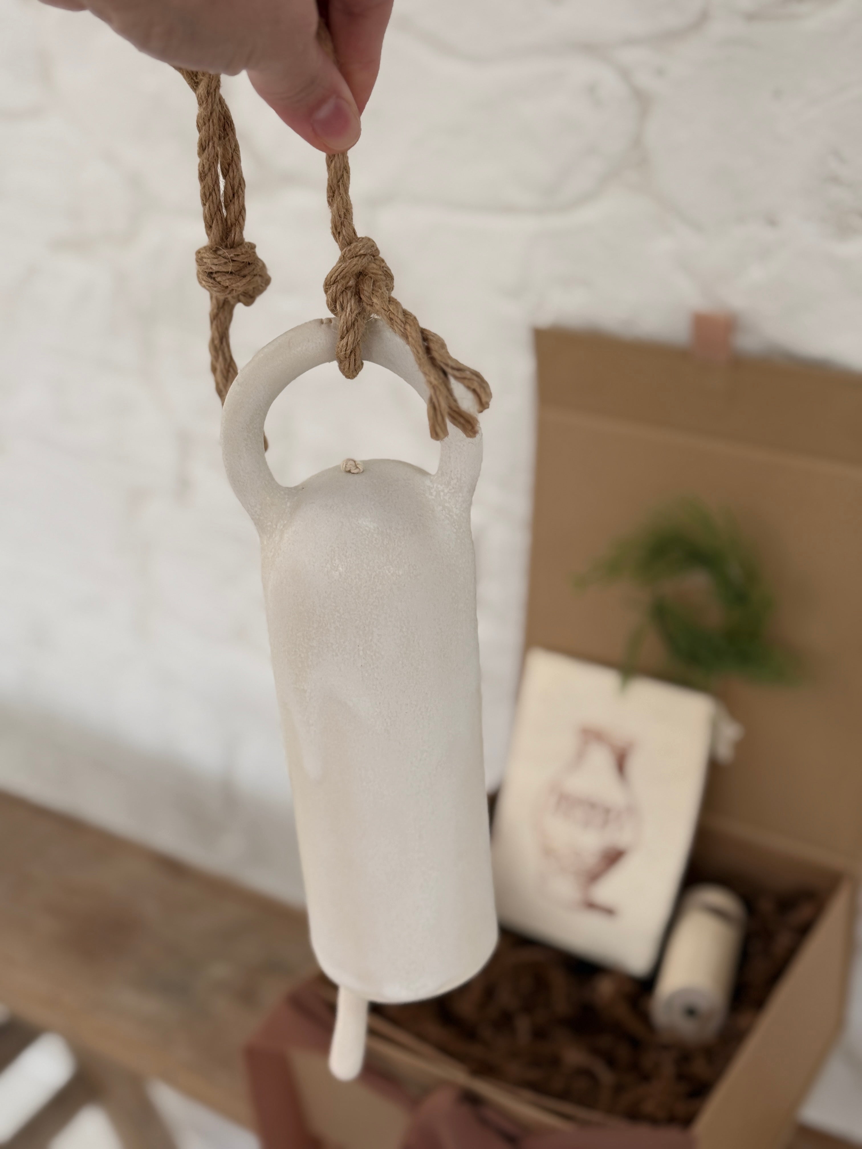 Long handmade ceramic bell in a frost white finish with a solid wood wall peg.