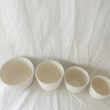 Overhead view of gloss white ceramic cups in graduated sizes, showing their glossy glazed interiors.