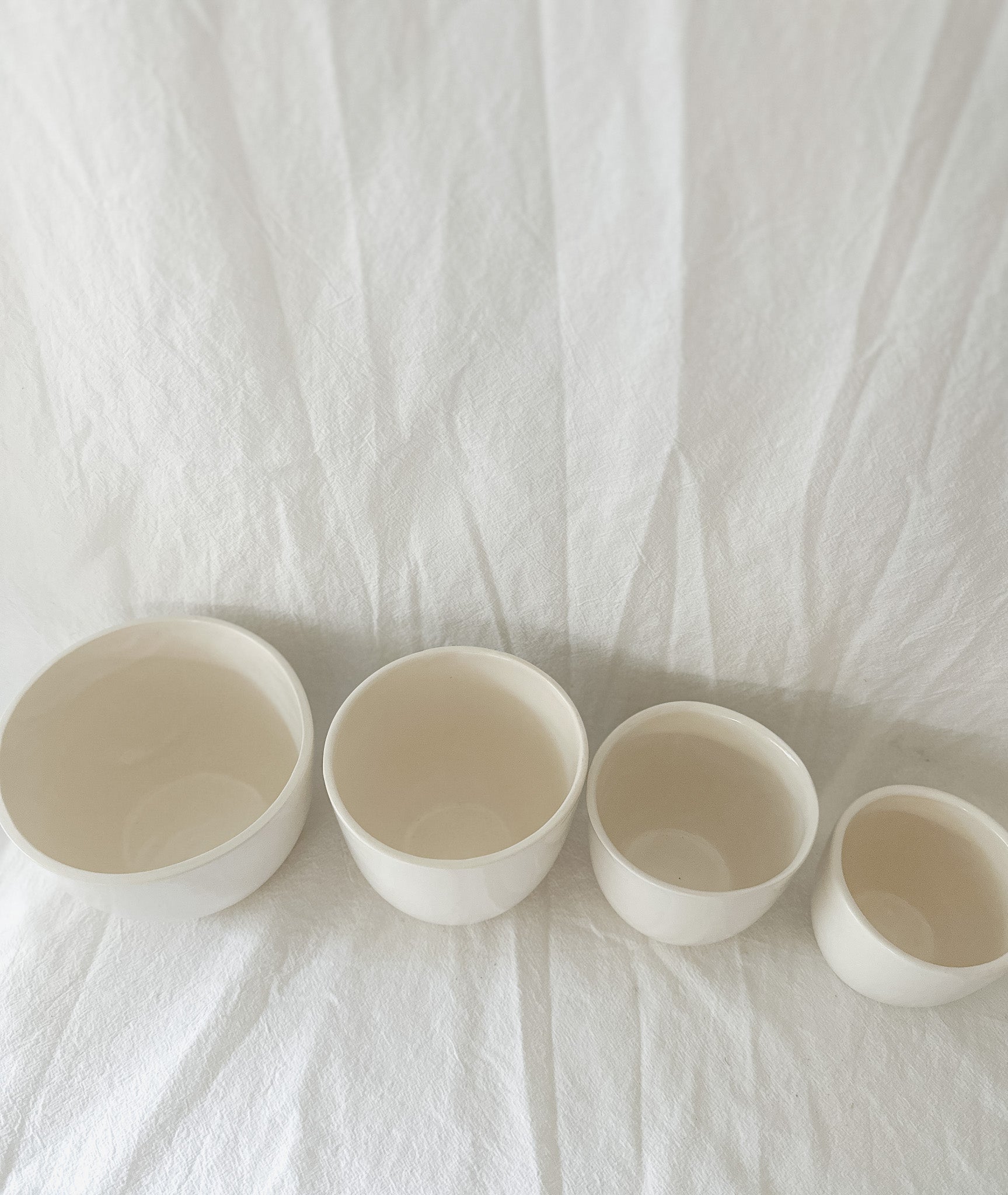 Overhead view of gloss white ceramic cups in graduated sizes, showing their glossy glazed interiors.