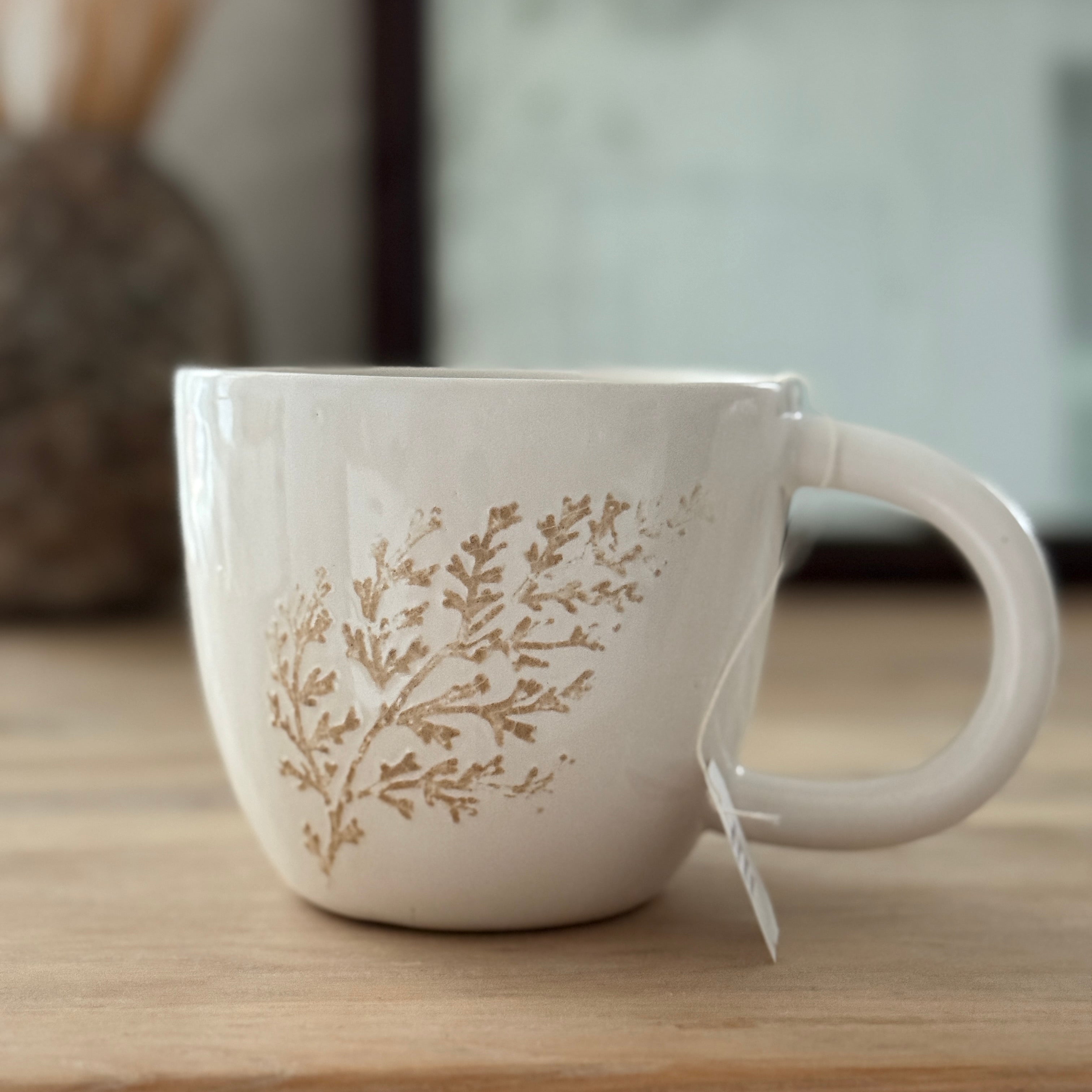 Handmade ceramic mug with a real leaf impression in sandy clay and a glossy white finish.