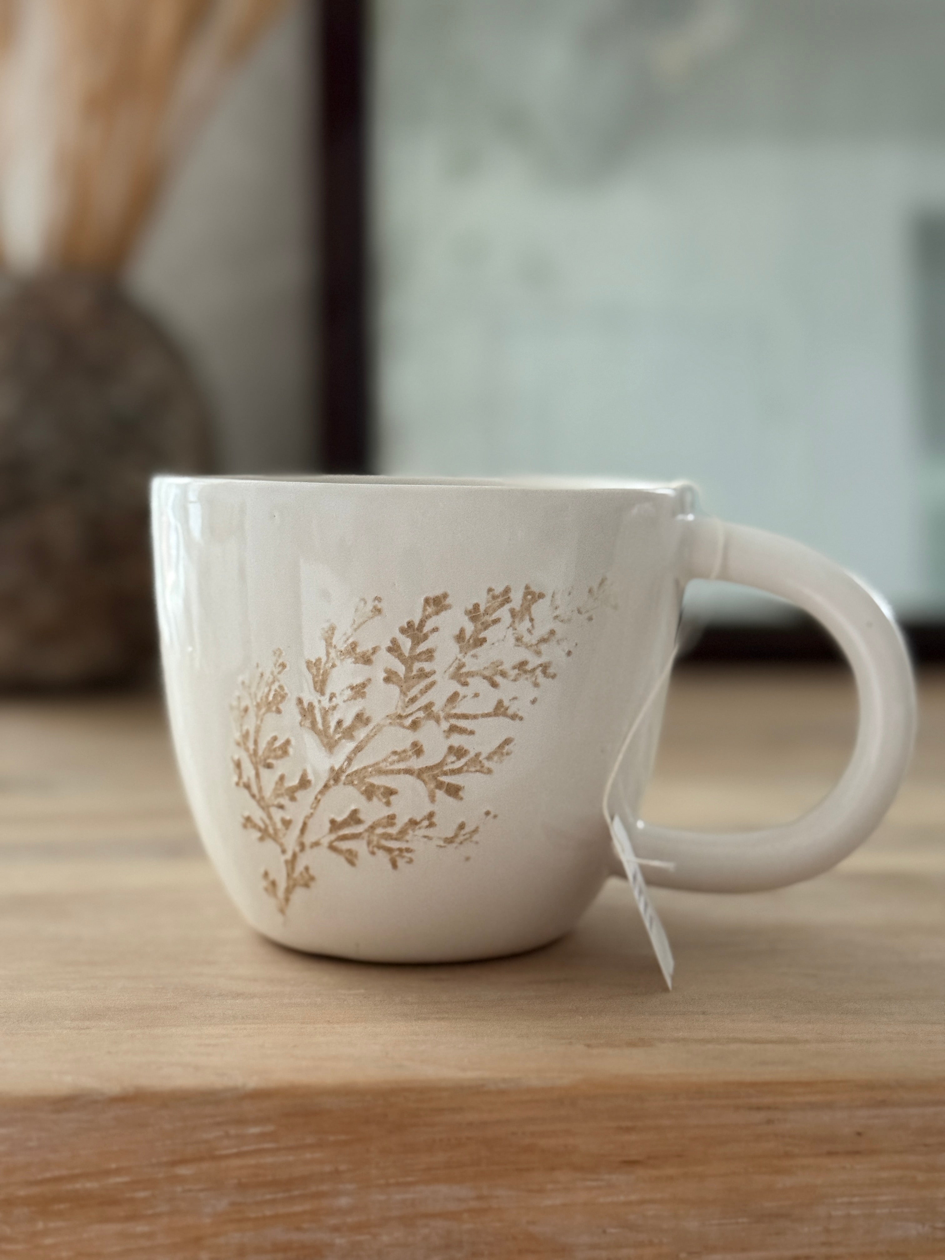 Handmade ceramic mug with a real leaf impression in sandy clay and a glossy white finish.