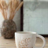 Handmade ceramic mug with a real leaf impression in sandy clay and a glossy white finish.
