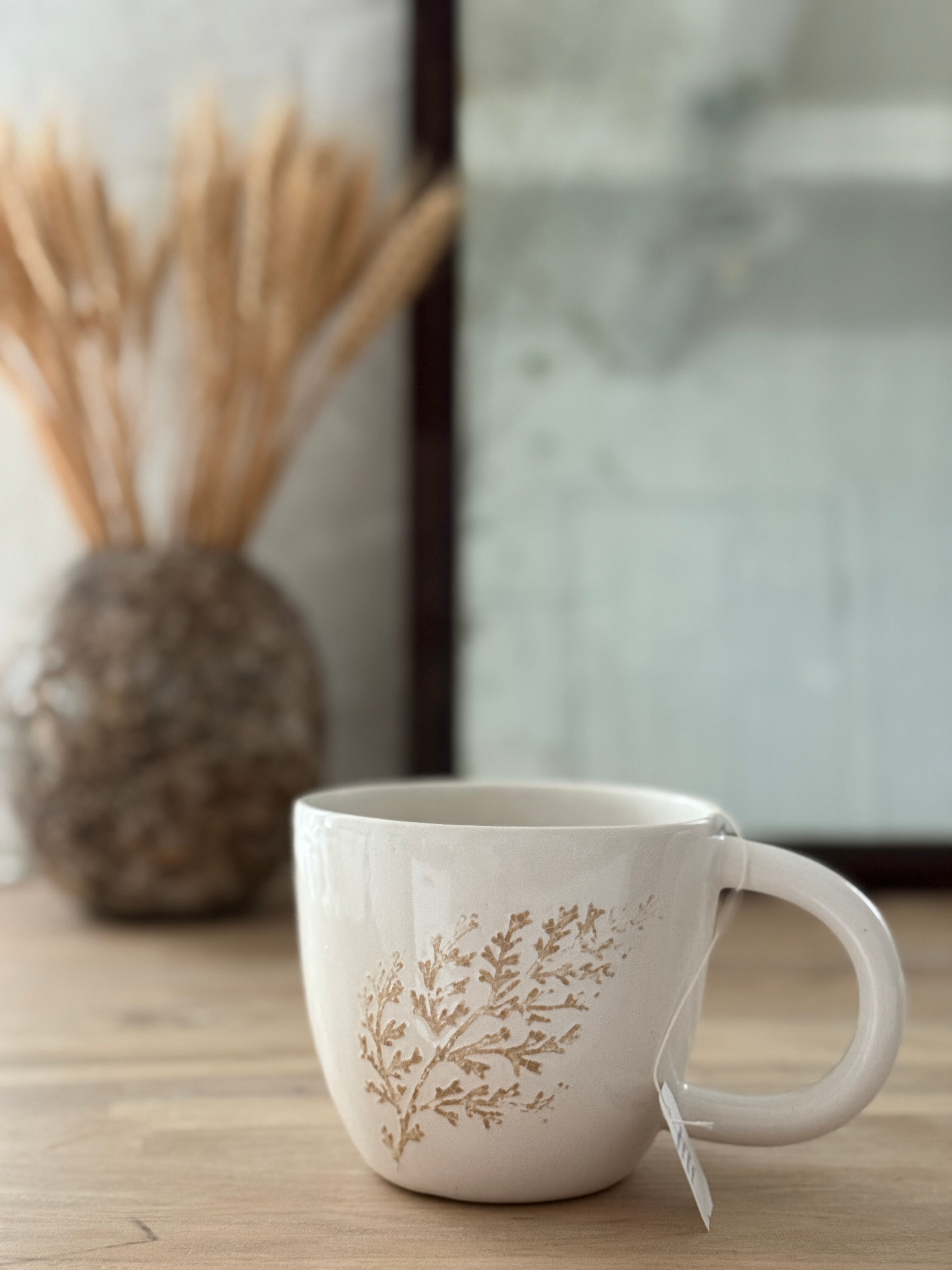Handmade ceramic mug with a real leaf impression in sandy clay and a glossy white finish.